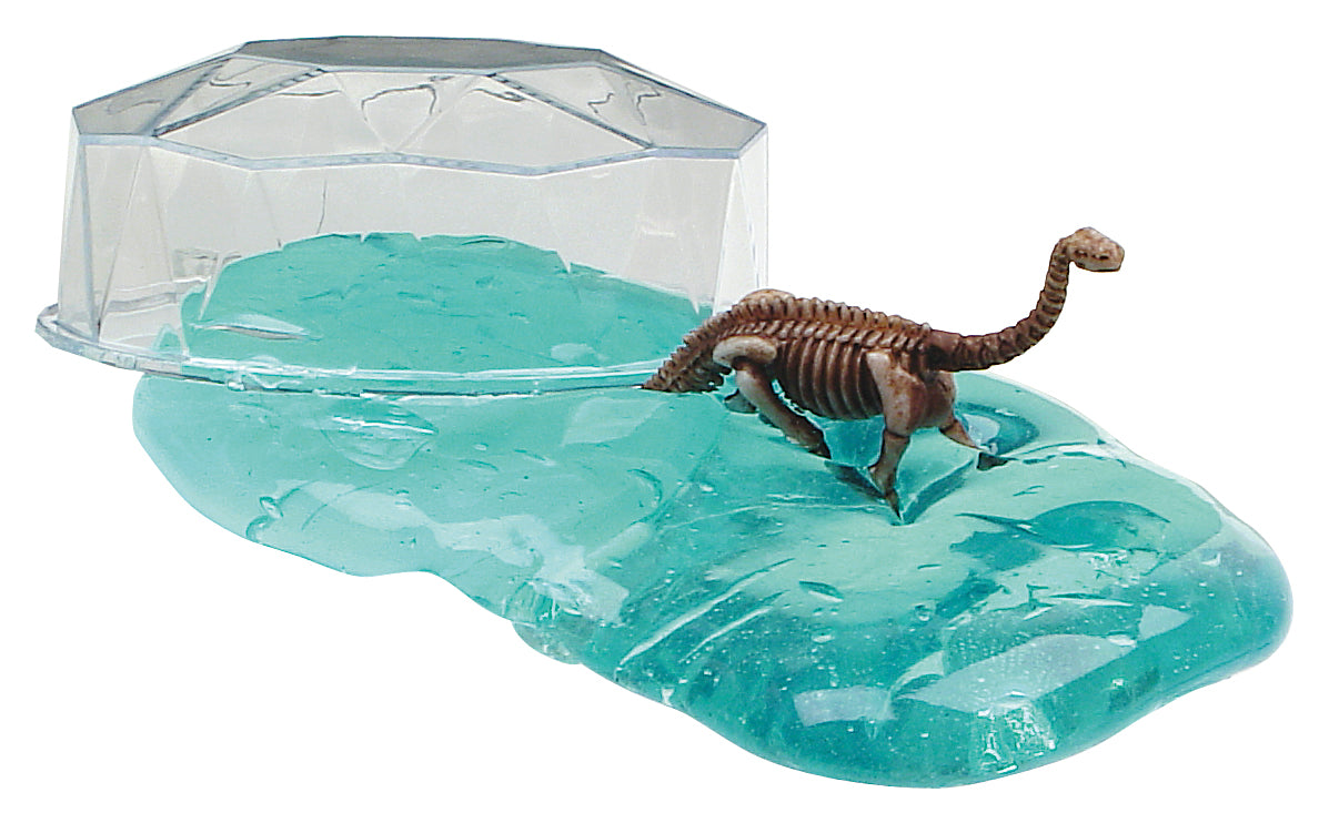 A Toysmith Colorful Dinosaur Fossil Putty figure stands on translucent blue putty next to a clear plastic "iceberg" structure, all by Toysmith.