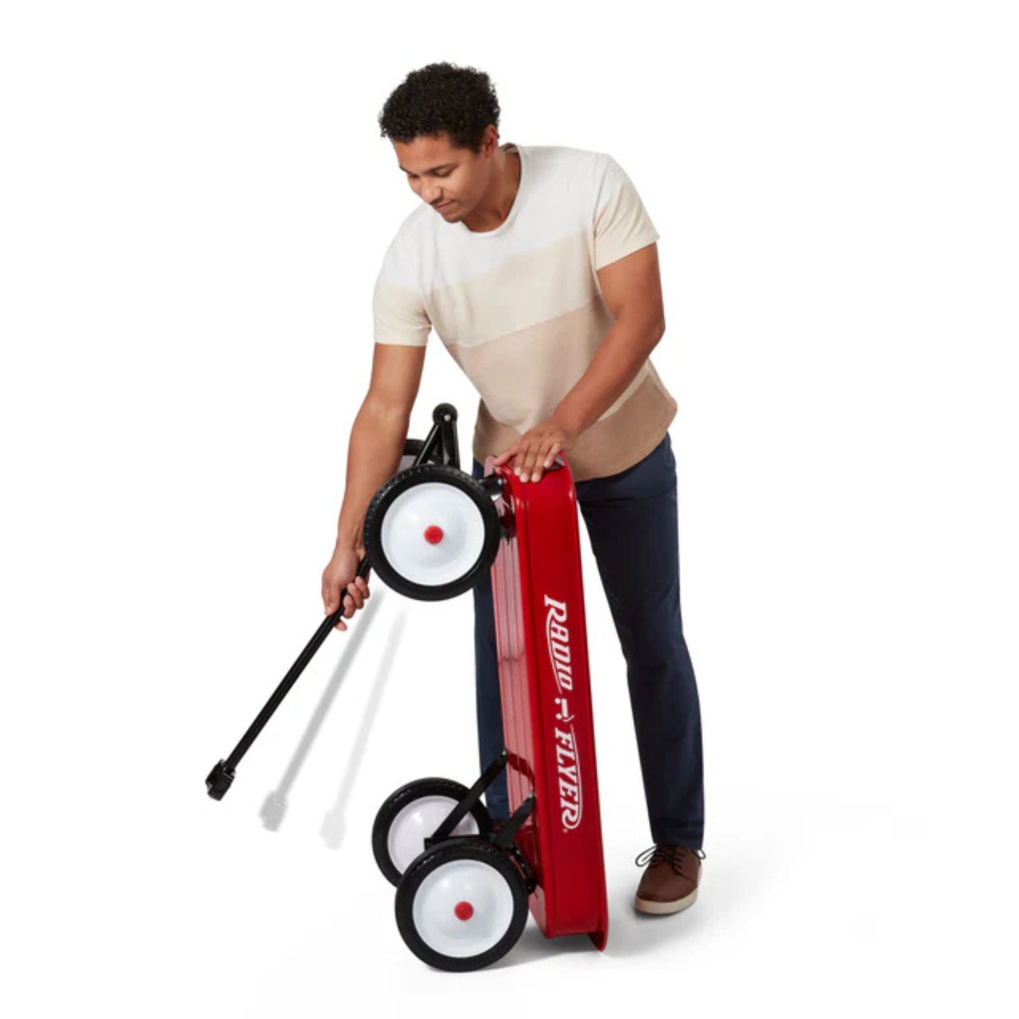 A person folds a Radio Flyer Classic Red Wagon with white wheels by holding its handle, set against a plain white background.