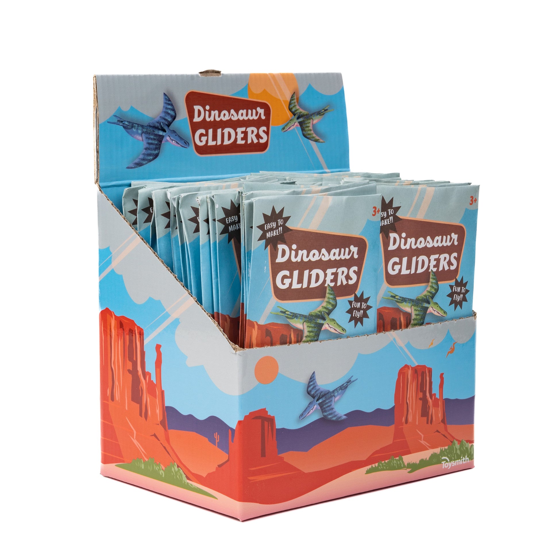 A vibrant display box holds multiple packs of Toysmith Dinosaur Gliders, Flying Toy by Toysmith, each featuring illustrated dinosaur airplanes soaring over a desert landscape with mesas and red rocks on the packaging.