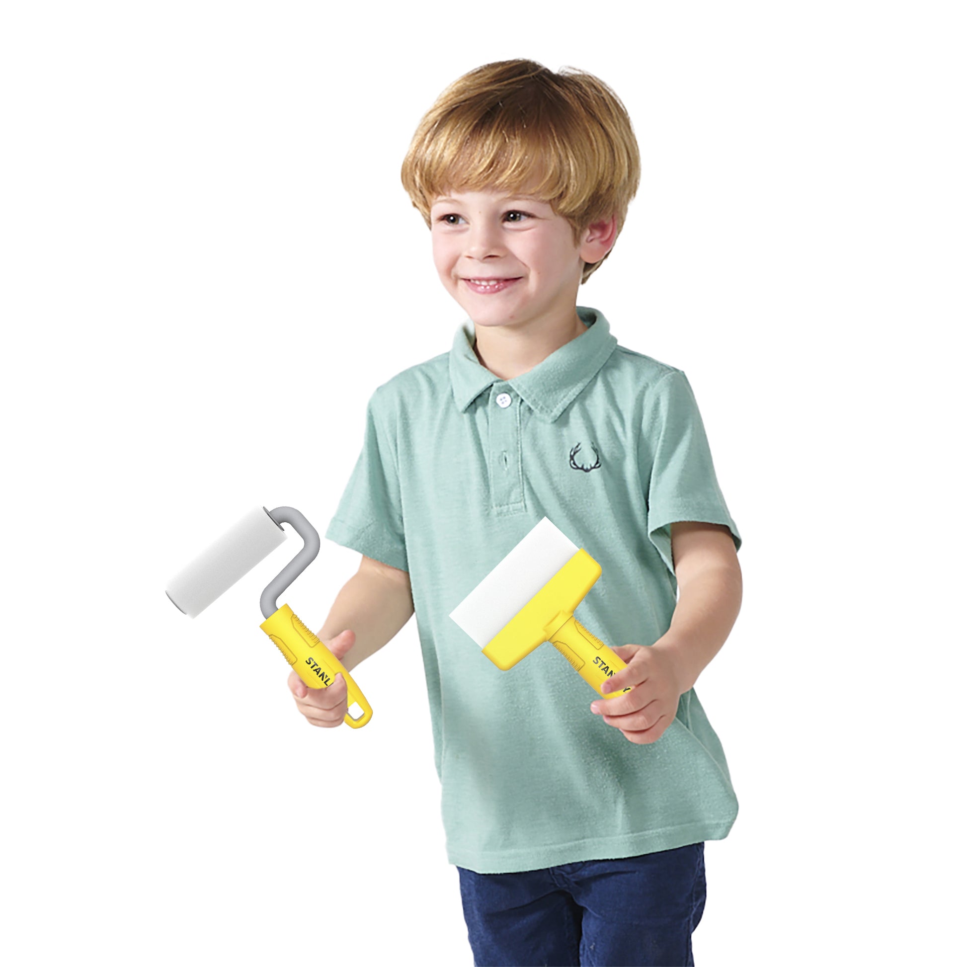 A young boy with light brown hair, dressed in a light green polo and blue pants, smiles while holding two yellow Stanley Jr. Deluxe Kid's Painters Set rollers by Red Toolbox against a plain white background.