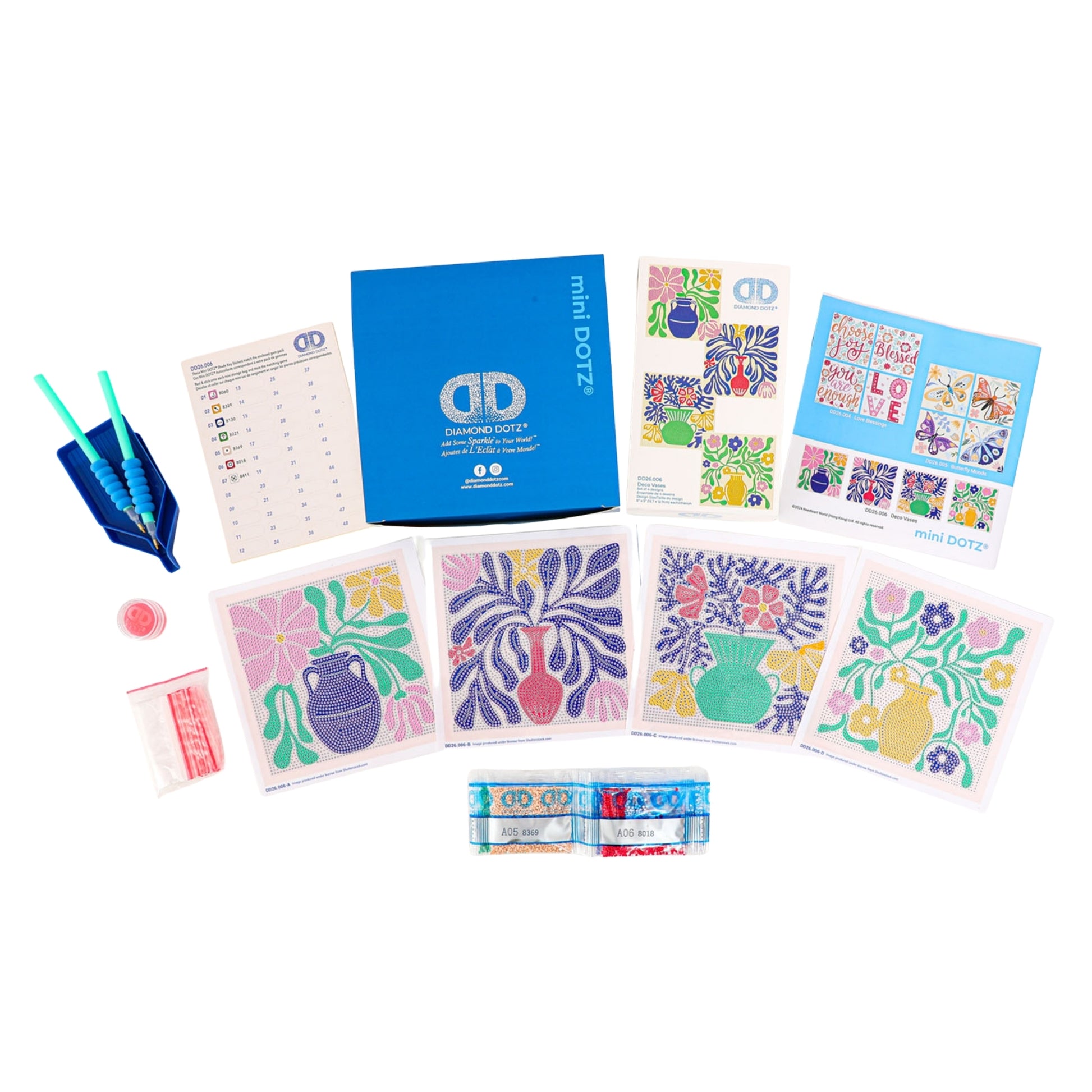 The Diamond Dotz Mini Dotz kit includes a blue box, four floral canvas cards, colored diamond beads in tubes, tools, wax, an instruction sheet, and a reference guide displayed neatly on a white surface.
