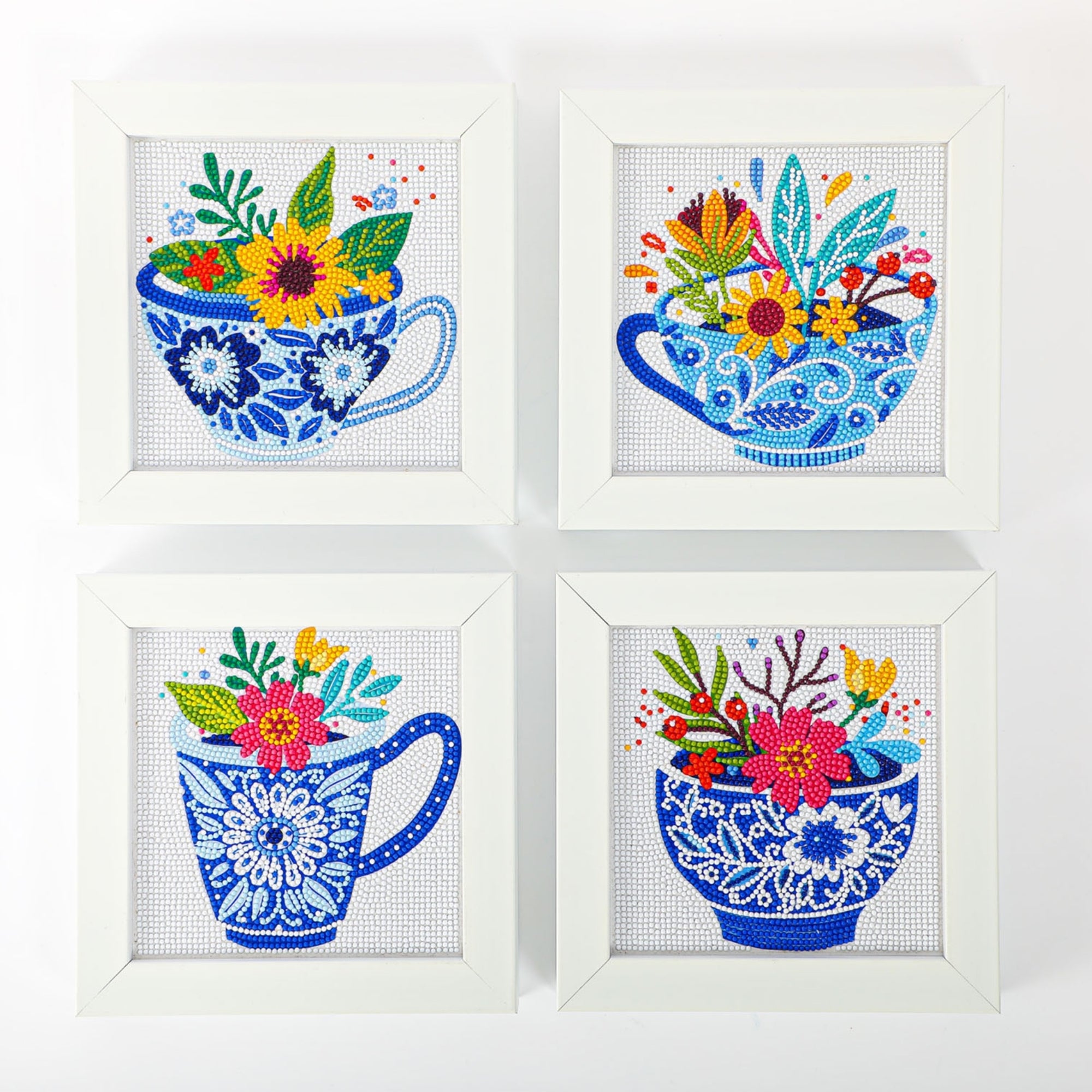 Four white-framed Diamond Dotz Mini Dotz artworks display blue teacups with intricate floral patterns, each brimming with colorful flowers and leaves, arranged in a two-by-two grid on a white background.