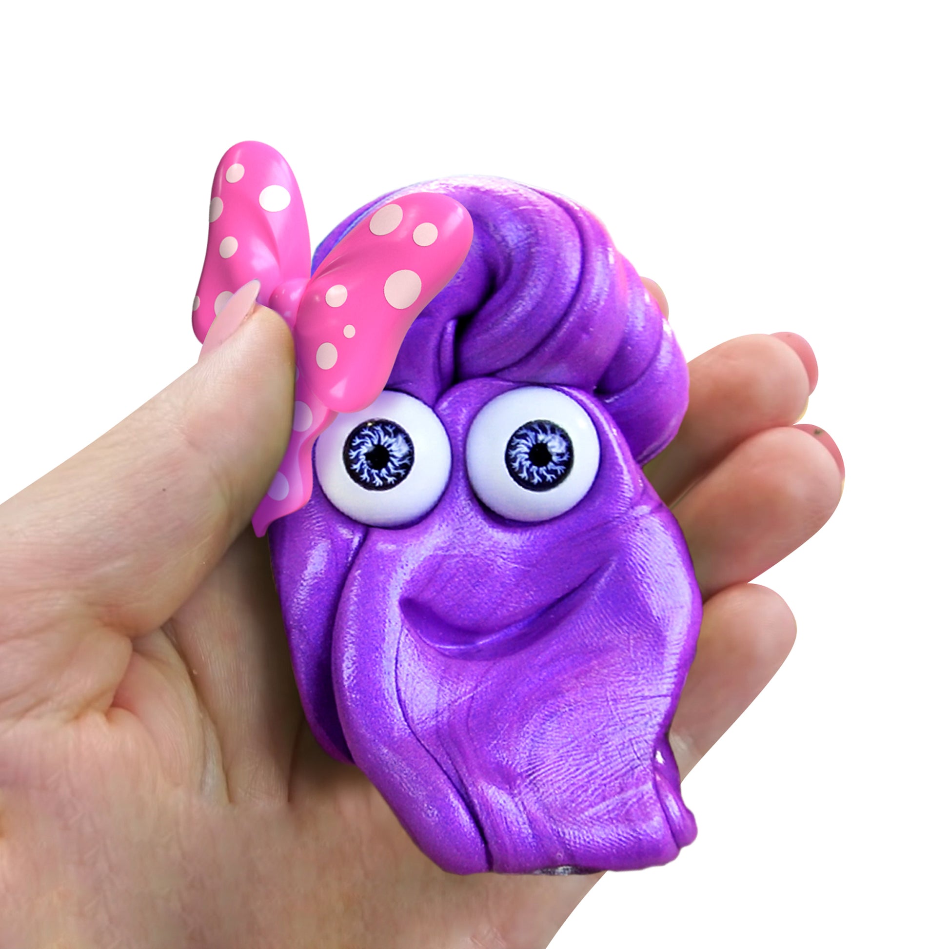 A hand holds a small, purple, cartoon-like clay figure with big eyes, a pink polka-dot bow, and a smiling mouth from the Doctor Squish Putty Buddies Asst. 21ct CDU against a white background.