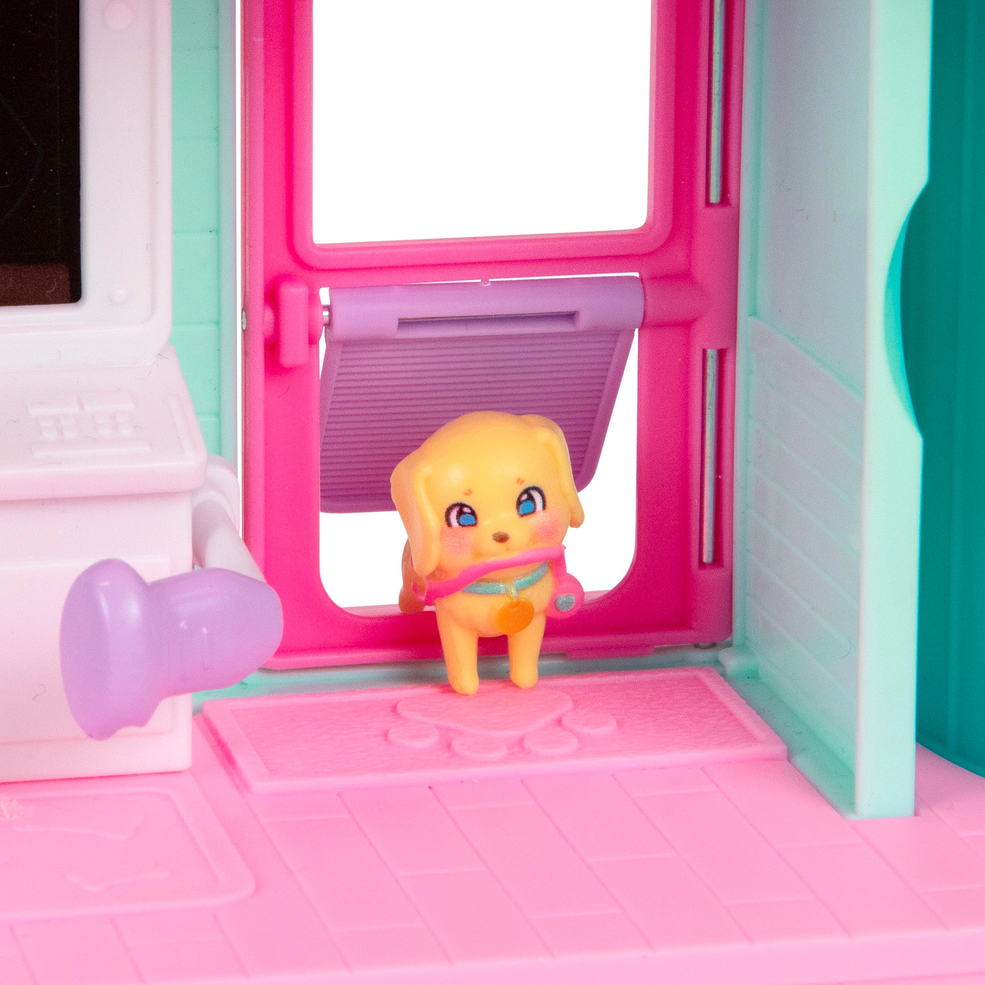 A small yellow toy dog with a pink collar stands on a pink mat inside the colorful LLP Mama Surprise Families Veterinarian Playset, near a pink door with a purple flap.