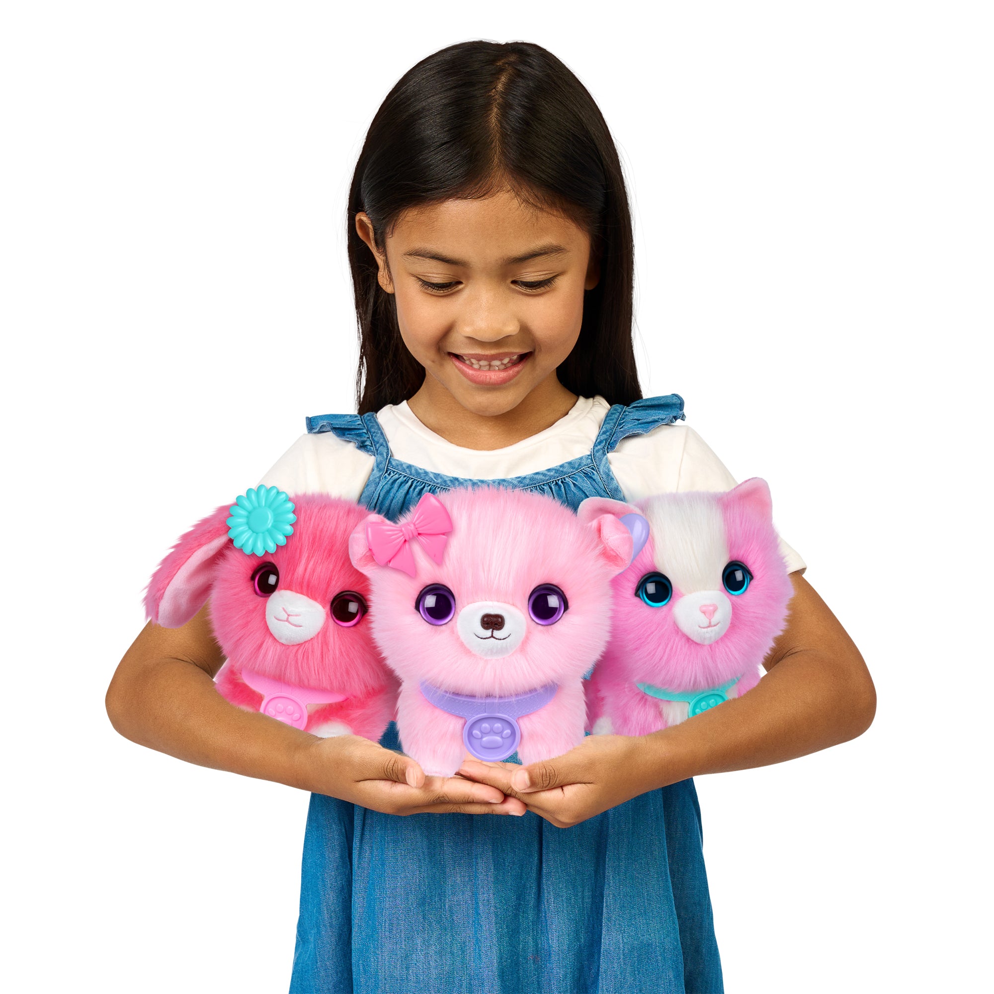 A young girl smiles while holding three Scruff A Luvs Single Pet Assortment plush animals from Moose Toys: a pink bunny with a blue flower, a pink dog with a bow, and a pink-and-white cat, all rescue toys with big shiny eyes.