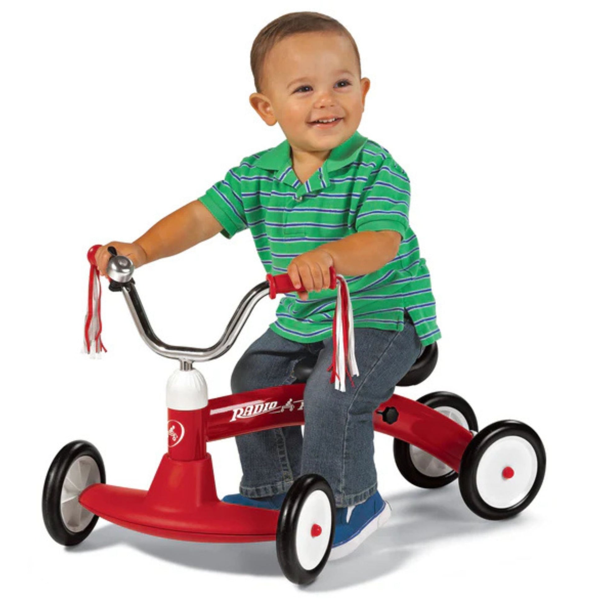 A smiling toddler in a green striped shirt and jeans rides the Radio Flyer Scoot About by Radio Flyer, featuring white wheels and handlebar streamers, against a white background.