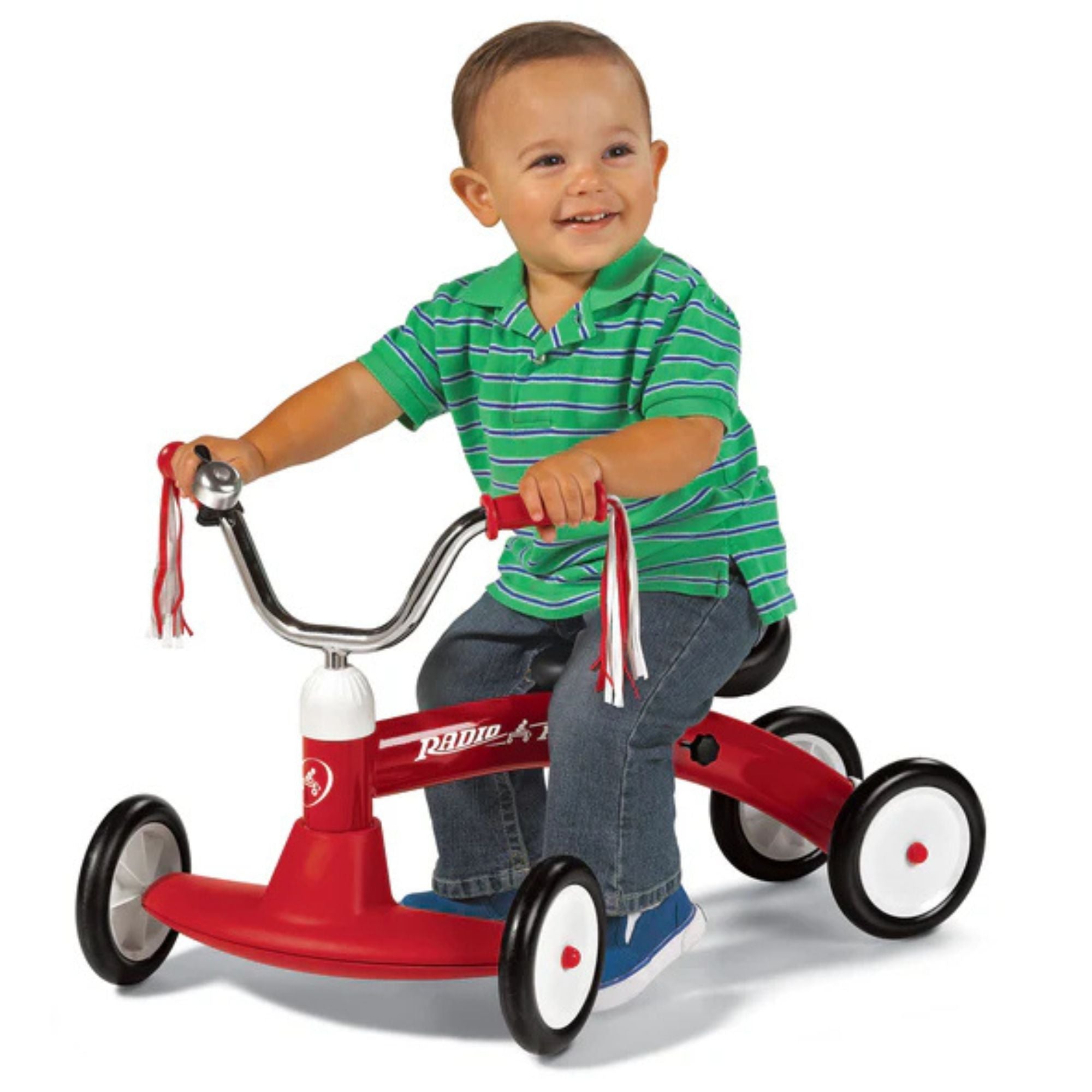 A smiling toddler in a green striped shirt and jeans rides the Radio Flyer Scoot About by Radio Flyer, featuring white wheels and handlebar streamers, against a white background.