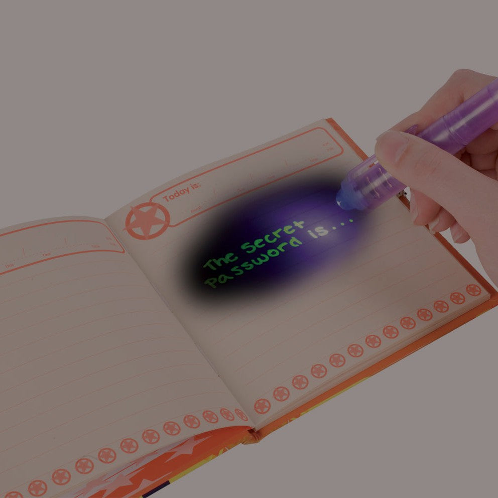 A hand uses the IQ 2 in 1 Invisible Writer’s purple UV light to reveal a secret message in a journal. The writing, “The Secret Password Is…” glows on the lined page when illuminated by the special pen’s light.