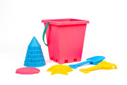 The Toysmith 6pc Set Pink Sand Bucket Set includes a pink bucket with green handle, blue cone, yellow star, red shell molds, a blue shovel, and yellow rake—all by Toysmith, shown on a white background.