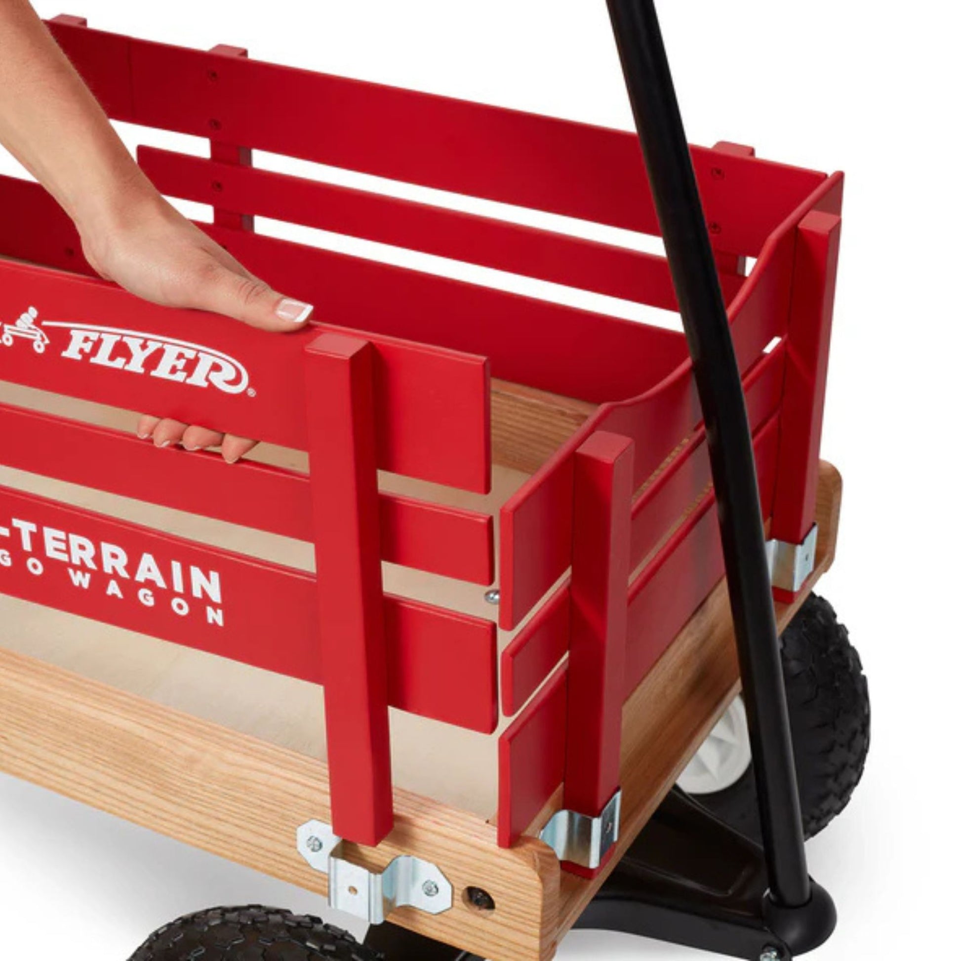 A hand lifts the side panel of a red Radio Flyer All Terrain Cargo Wagon with black wheels and handle. The wagon features the "FLYER" logo and "ALL TERRAIN CARGO WAGON" written on its side.