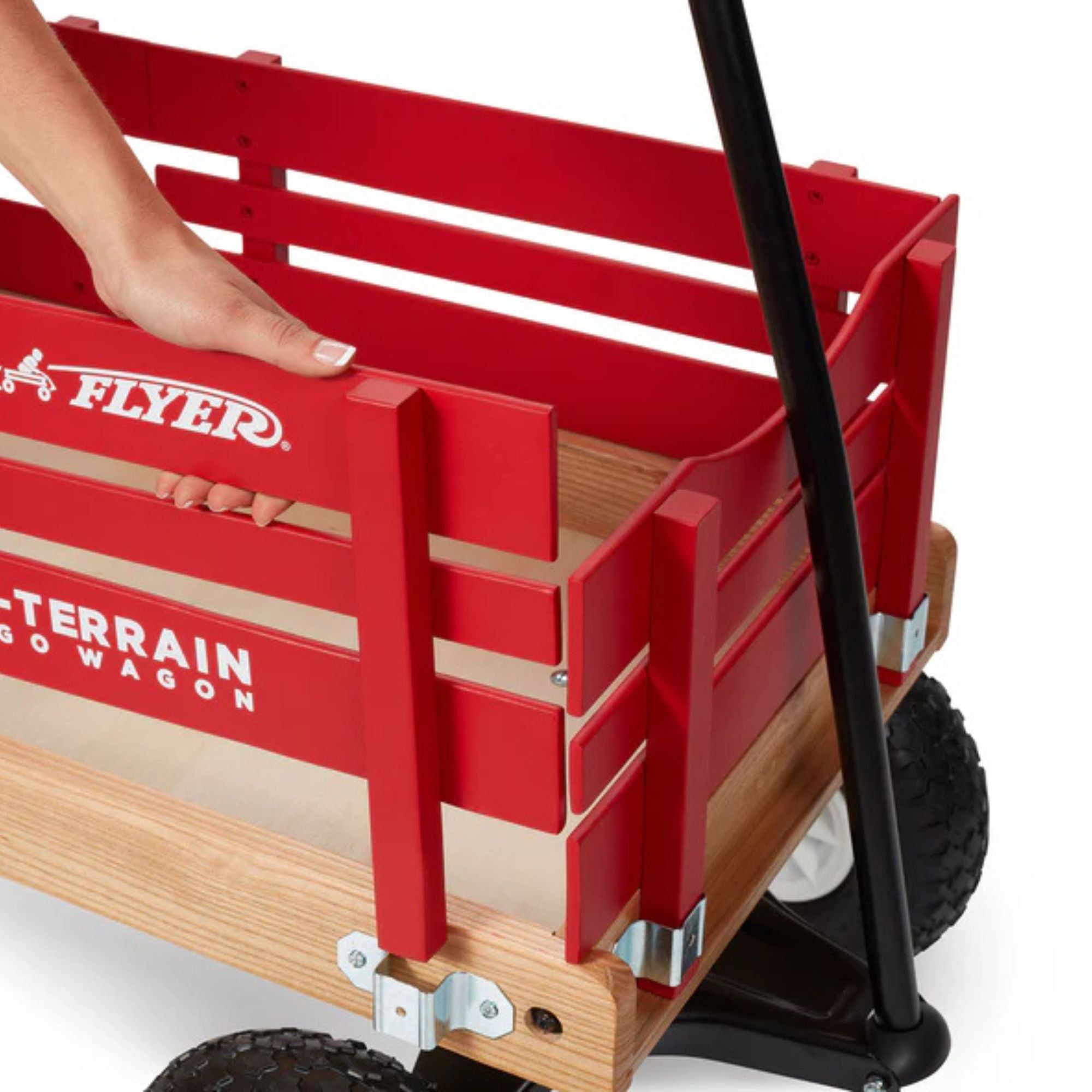 A hand lifts the side panel of a red Radio Flyer All Terrain Cargo Wagon with black wheels and handle. The wagon features the "FLYER" logo and "ALL TERRAIN CARGO WAGON" written on its side.