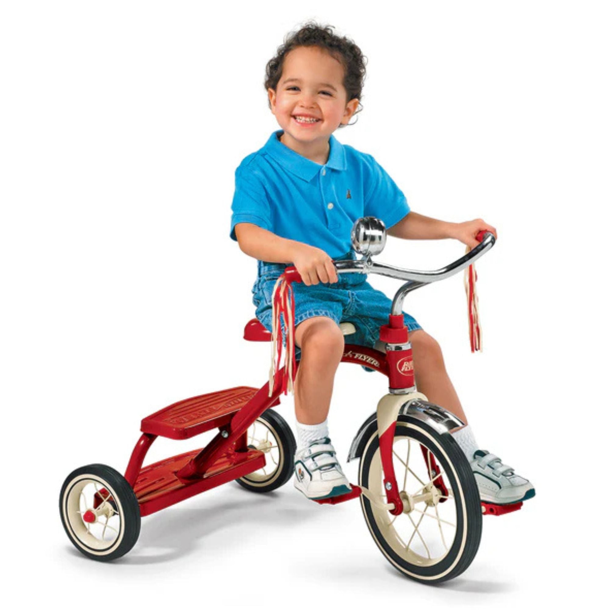A smiling young child in blue rides the Radio Flyer Classic Red Dual Deck Tricycle by Radio Flyer, featuring handlebar tassels, against a plain white background.