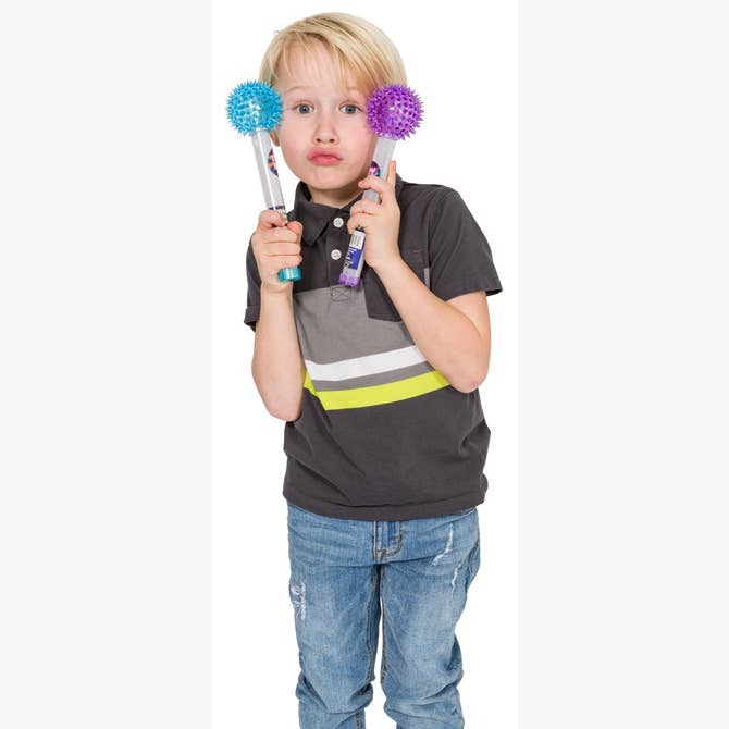 A young boy with blond hair in a dark polo and jeans playfully holds two Astroverse Cosmic Ray Light-Up Wands, blue and purple, near his face like glasses—fun party favors from Astroverse for endless entertainment.
