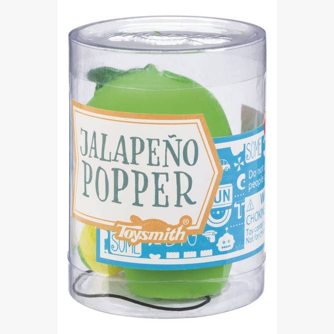 A clear plastic container labeled Toysmith Jalapeno Popper contains a green Jalapeno Popper fidget toy. The food-themed packaging features blue and white graphics and includes safety warnings.