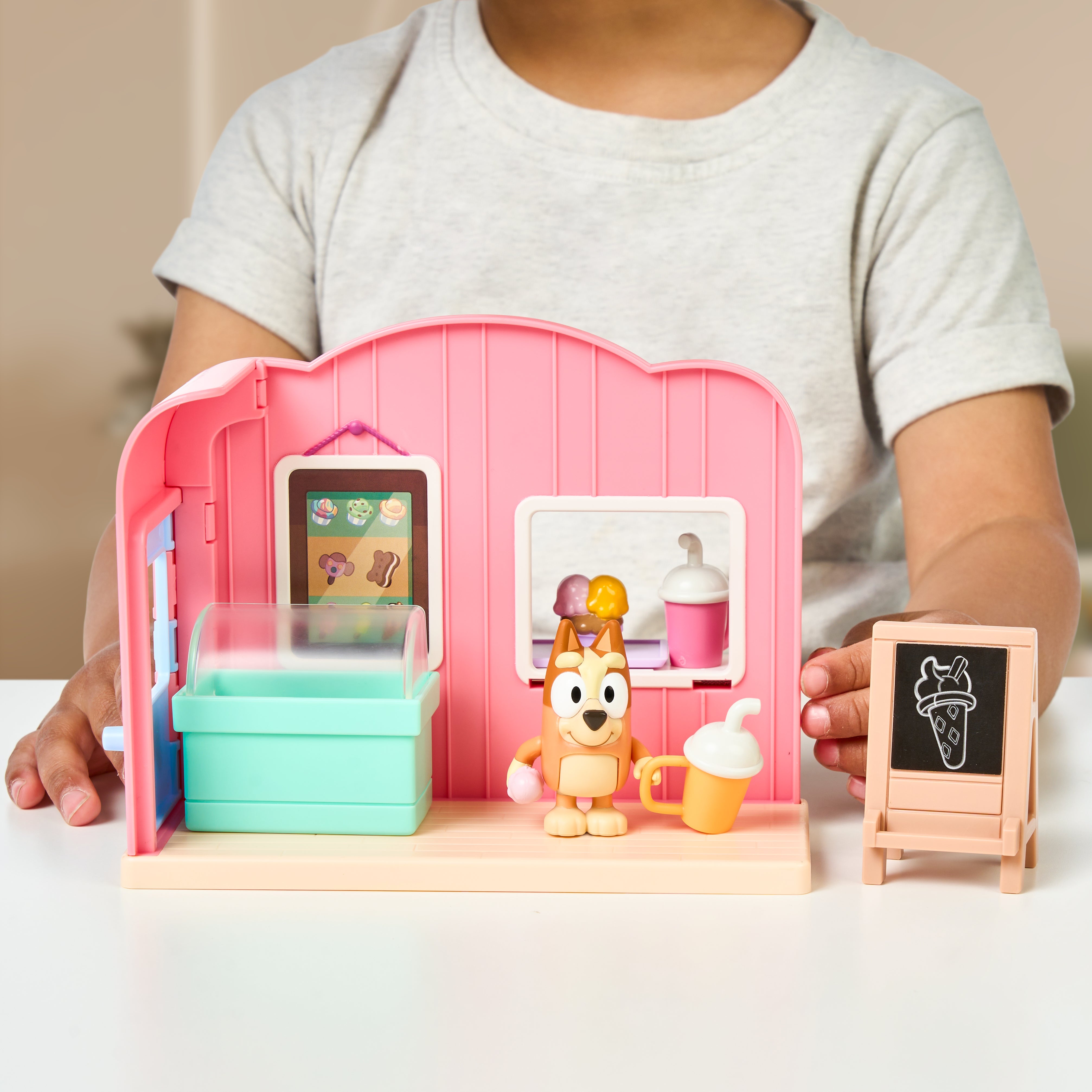 Child playing with a toy ice cream shop set on a table.