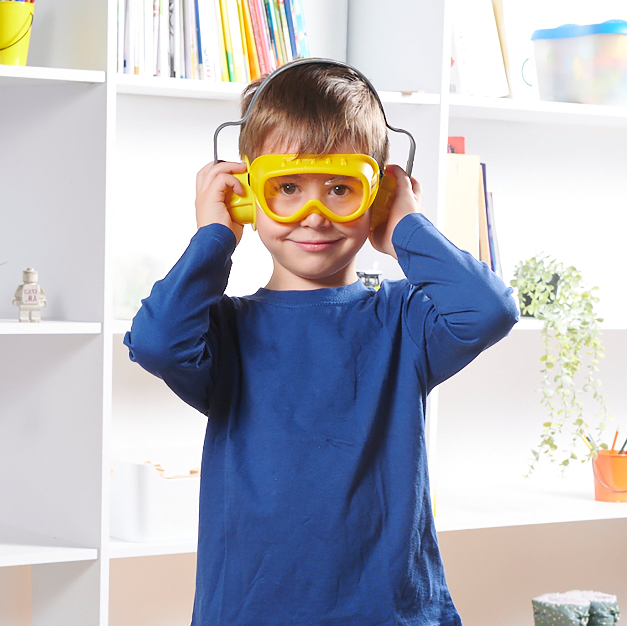 Child wearing yellow safety goggles in a room with shelves and books
