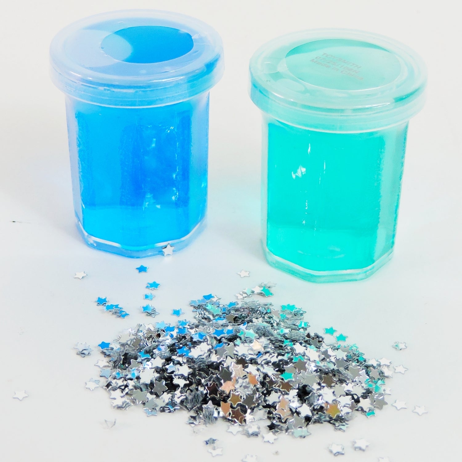 Two containers of blue glitter with a pile of multicolored glitter on a white background
