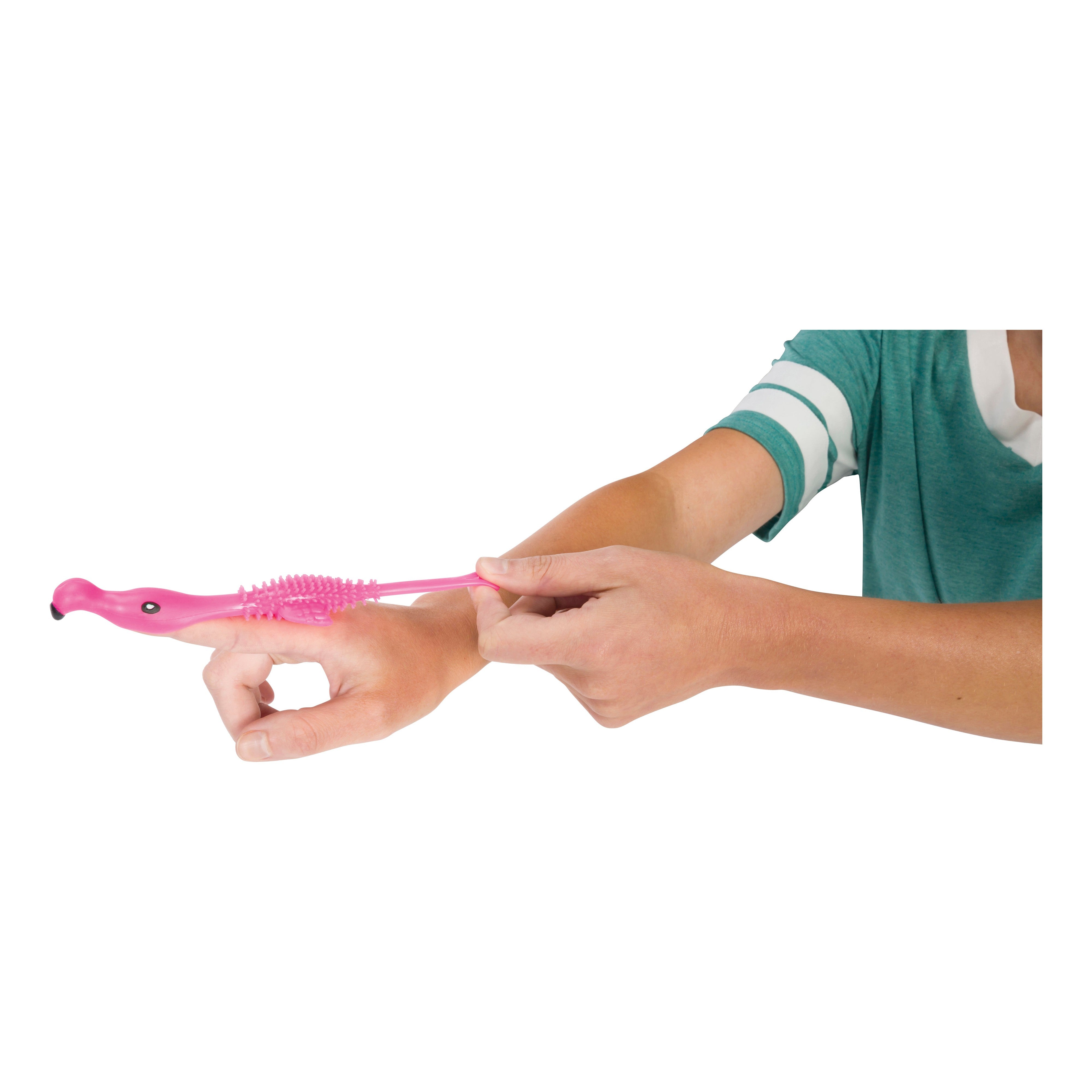 A person uses Toysmith's Flamingo Flingers—a pink, flamingo-shaped massager—on their forearm, holding it with one hand while the other arm is extended.