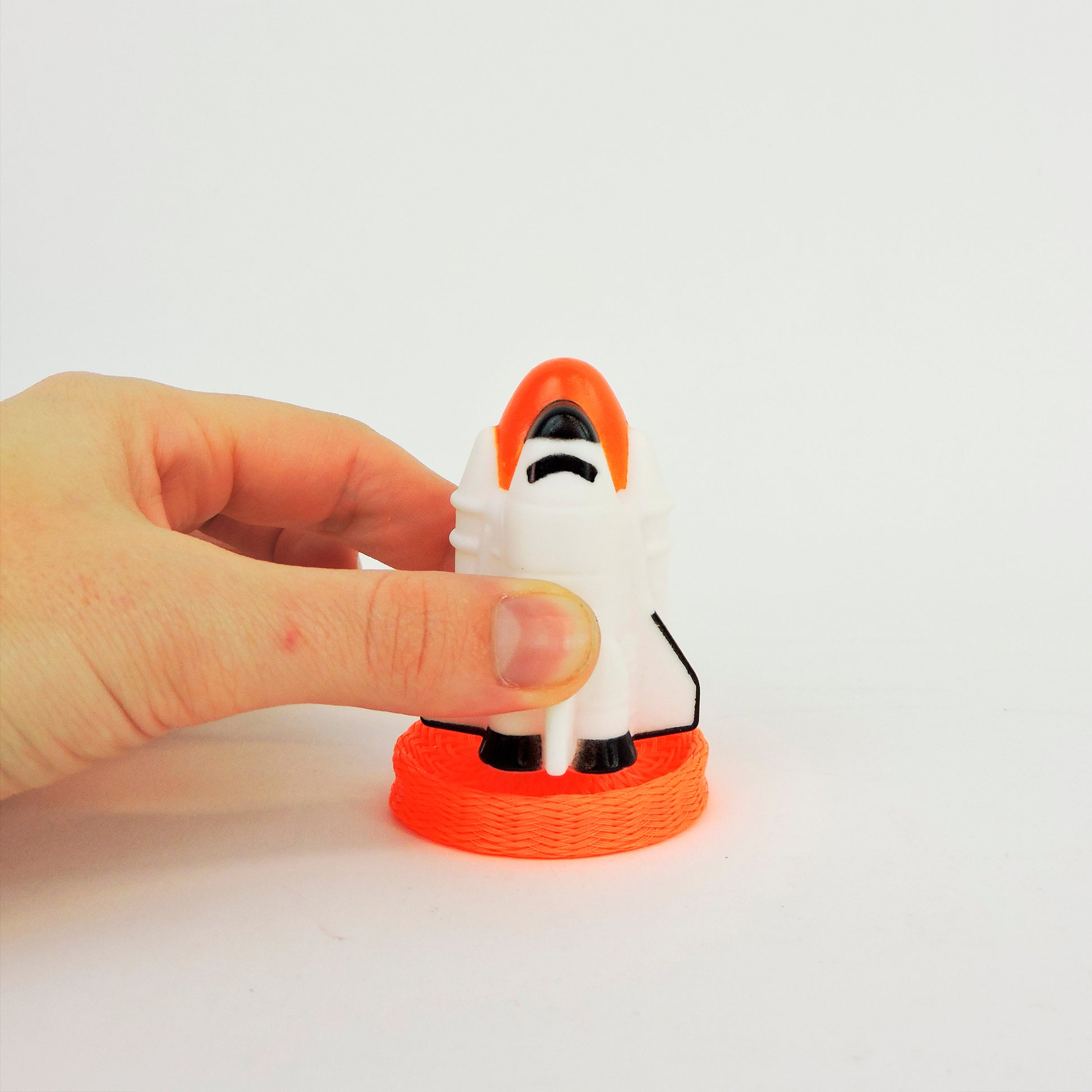 A hand holds the Astroverse Blast-Off Shuttle, a small white and orange toy rocket standing upright on an orange coil, set against a plain white background.