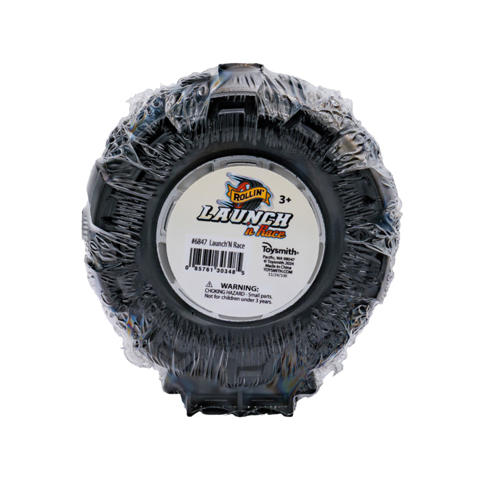 A round black Rollin' Launch 'N Race toy tire, wrapped in plastic and labeled for ages 3+. The center has a barcode and a choking hazard warning for under 3 years. Perfect for use with your favorite die-cast vehicle!.