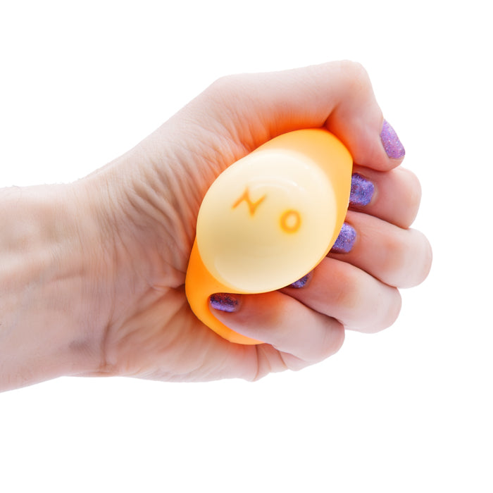 A hand with purple glittery nail polish squeezes a yellow Toysmith Squeezy Fortune Ball with "NO" printed on it, against a white background. This Toysmith fidget toy is perfect for stress relief and sensory play.