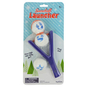 Toysmith Snowball Launcher by Toysmith: A winter toy set for ages 5+ with a purple slingshot and three white snowballs featuring cartoon snowman faces, ideal for kids or holiday party games, packaged against a snowy illustrated background.