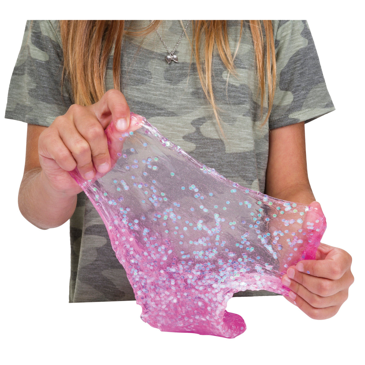 A person in a camouflage t-shirt stretches Toysmith Mix-Ins Slime Asst, a pink, clear slime with blue and white mix-ins. Only their hands and torso are visible. Brand: Toysmith.