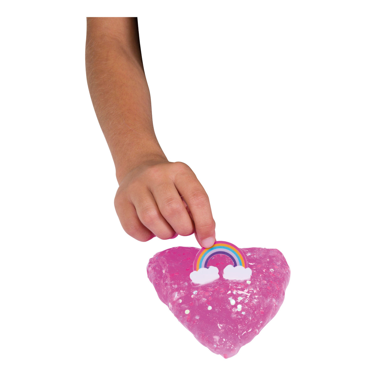 A child's hand presses a small rainbow into pink, glittery Toysmith Mix-Ins Slime Asst by Toysmith, with mix-ins, against a white background.