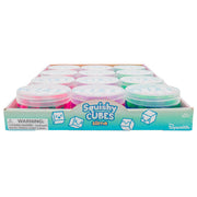 A Toysmith Squishy Cube Slime display box holds several round containers in pink and green, featuring cartoon cube characters and a choking hazard warning for small parts.