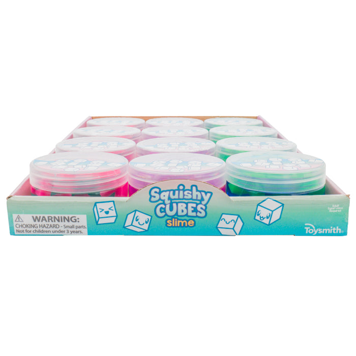 A Toysmith Squishy Cube Slime display box holds several round containers in pink and green, featuring cartoon cube characters and a choking hazard warning for small parts.