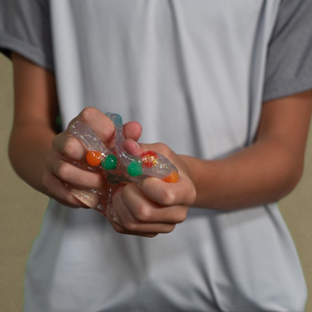 Someone squeezes Toysmith Polka Dot Slime with colorful foam beads in both hands, enjoying a fun sensory play experience.