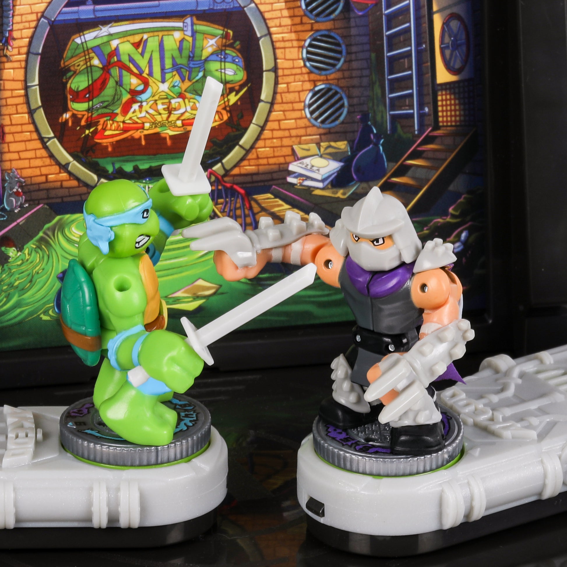 Two toy figures in front of a screen displaying 'Teenage Mutant Ninja Turtles' graphics.