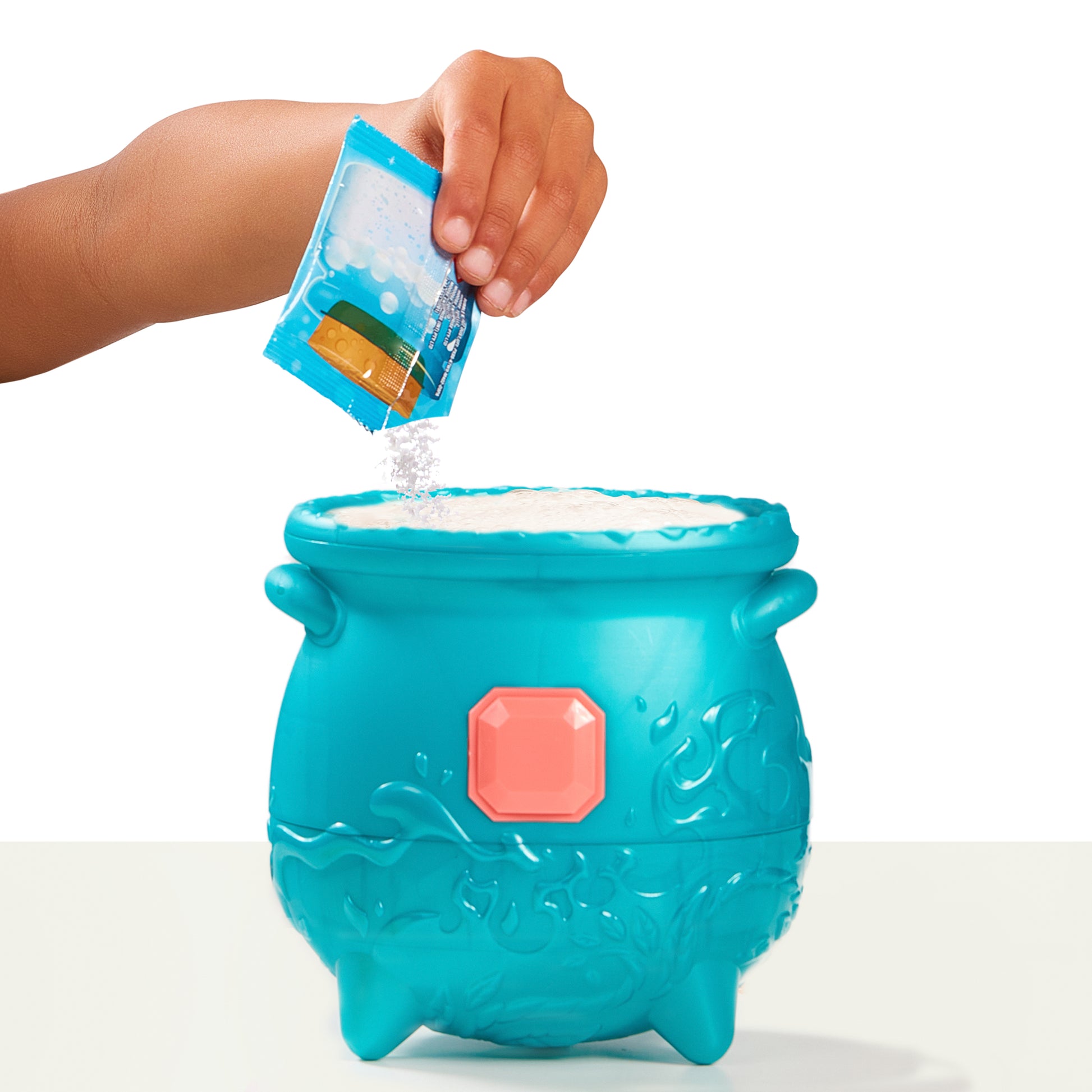 Blue toy cauldron with a hand pouring a packet of contents into it on a white background