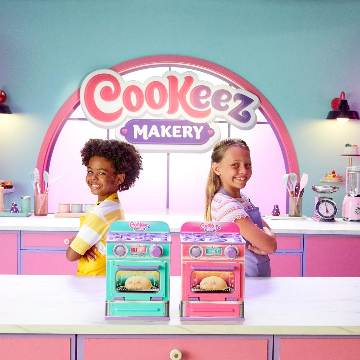 Two children in a toy kitchen set with 'CooKeez Makery' branding.