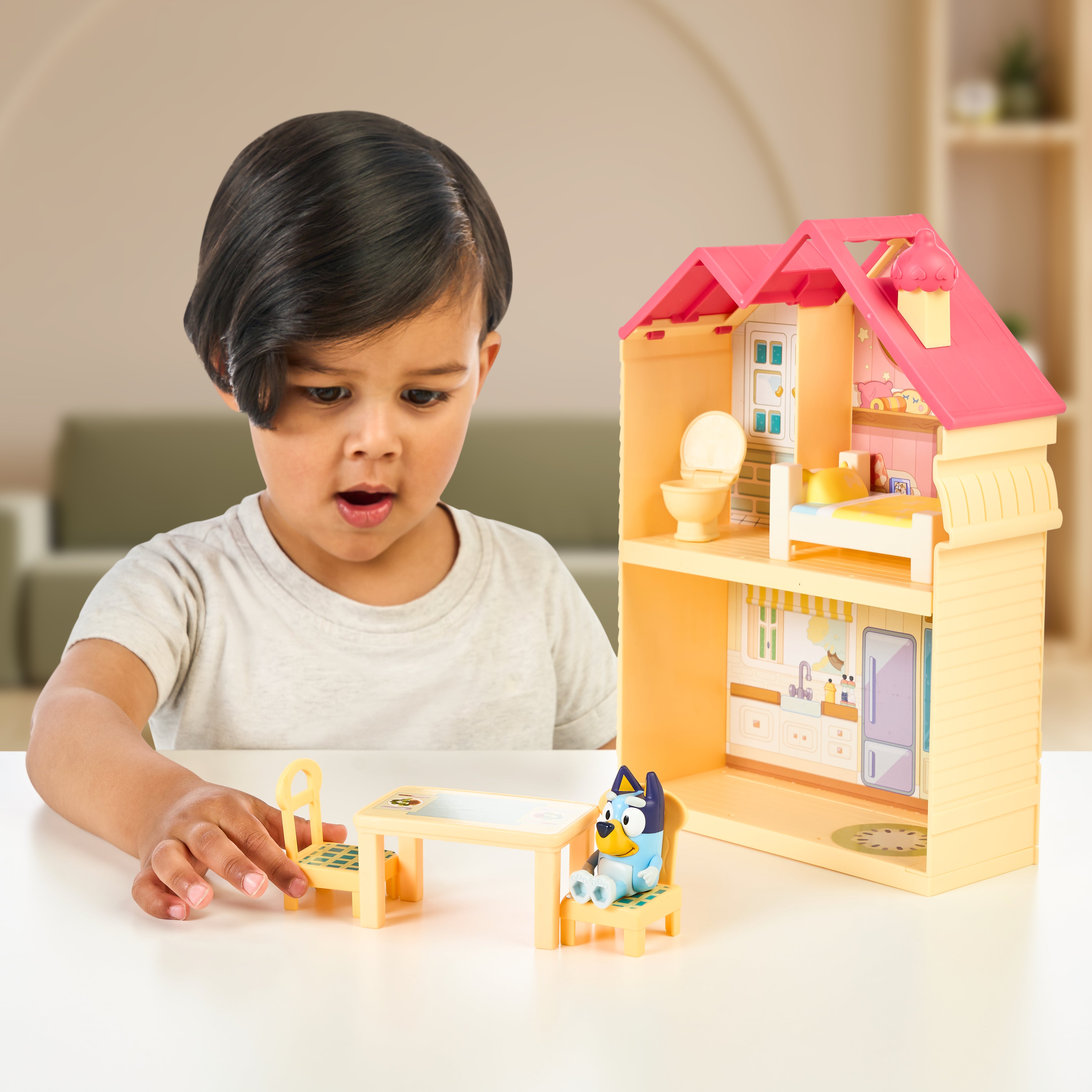 Child playing with a toy dollhouse and furniture on a table.