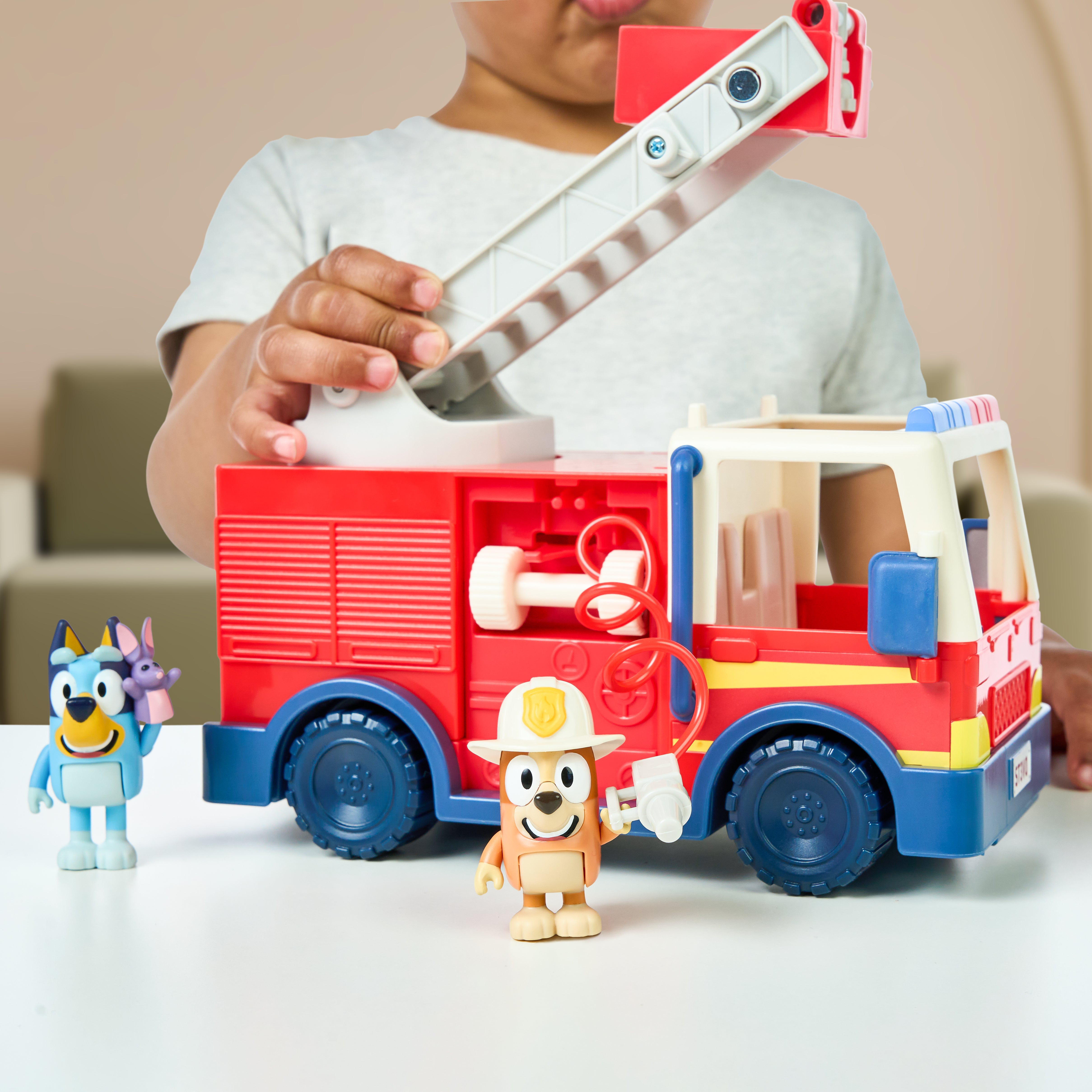 Child playing with a Bluey fire truck and figures on a white surface.