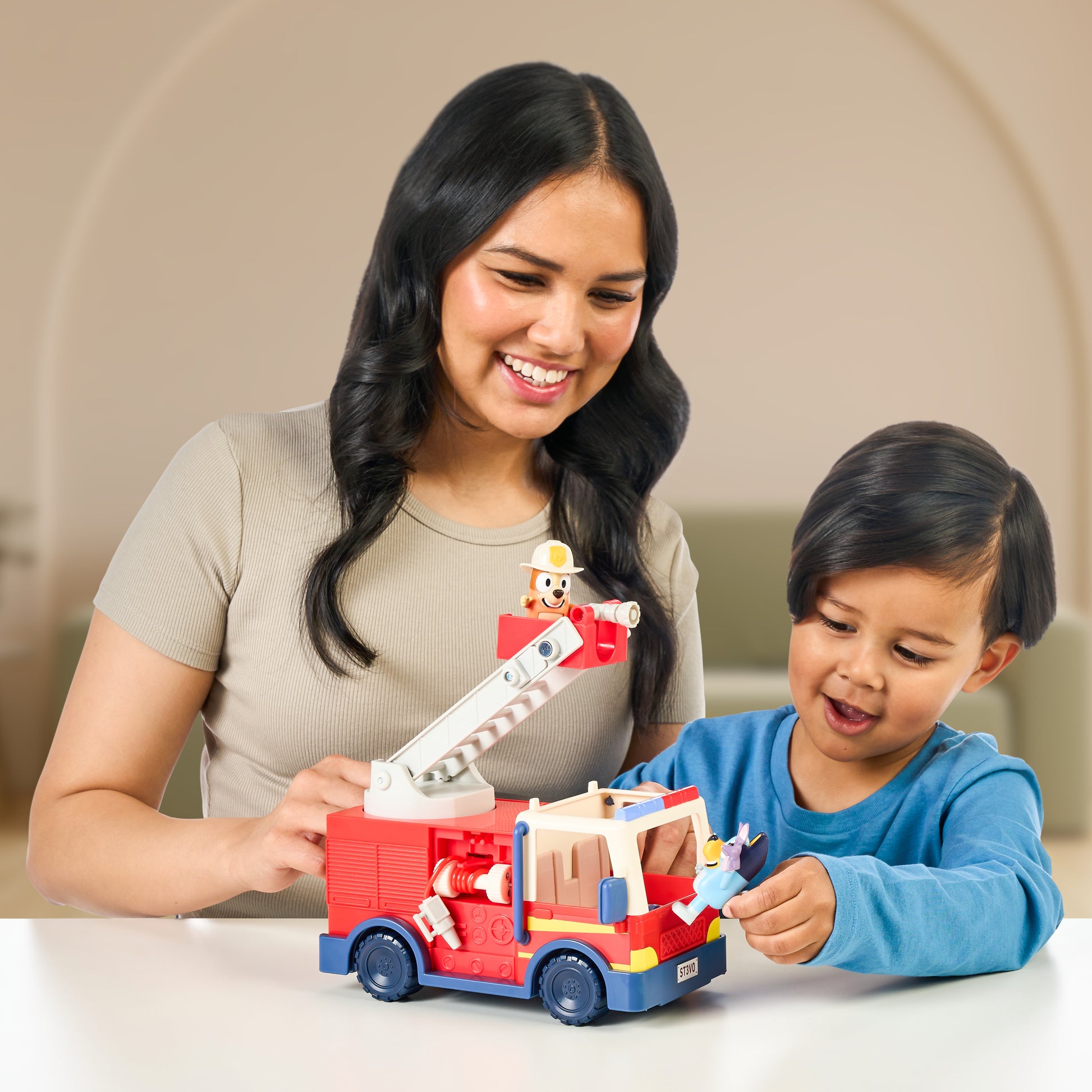 Woman and child playing with a toy fire truck set on a table.