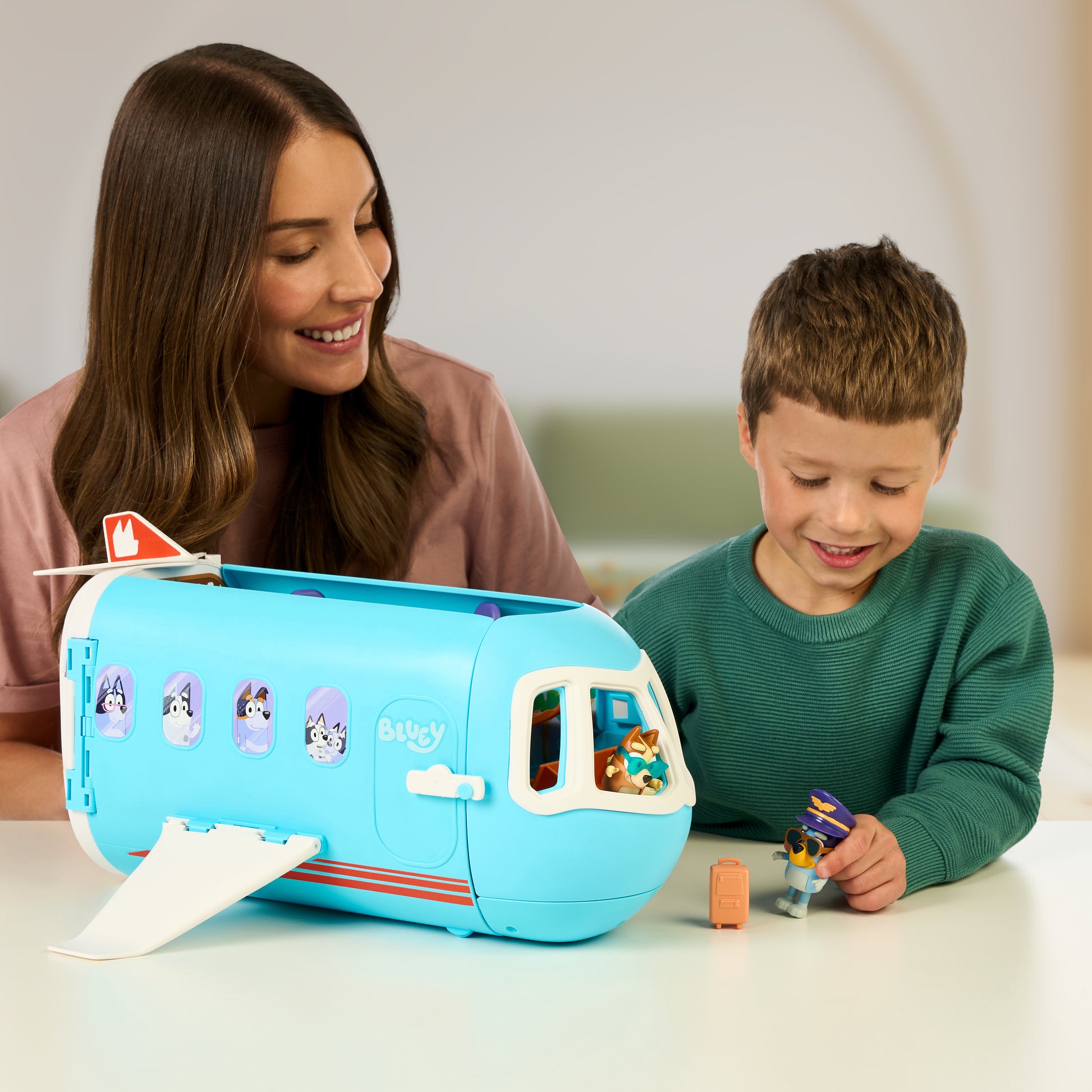 Woman and child playing with a blue toy camper and figures on a table.