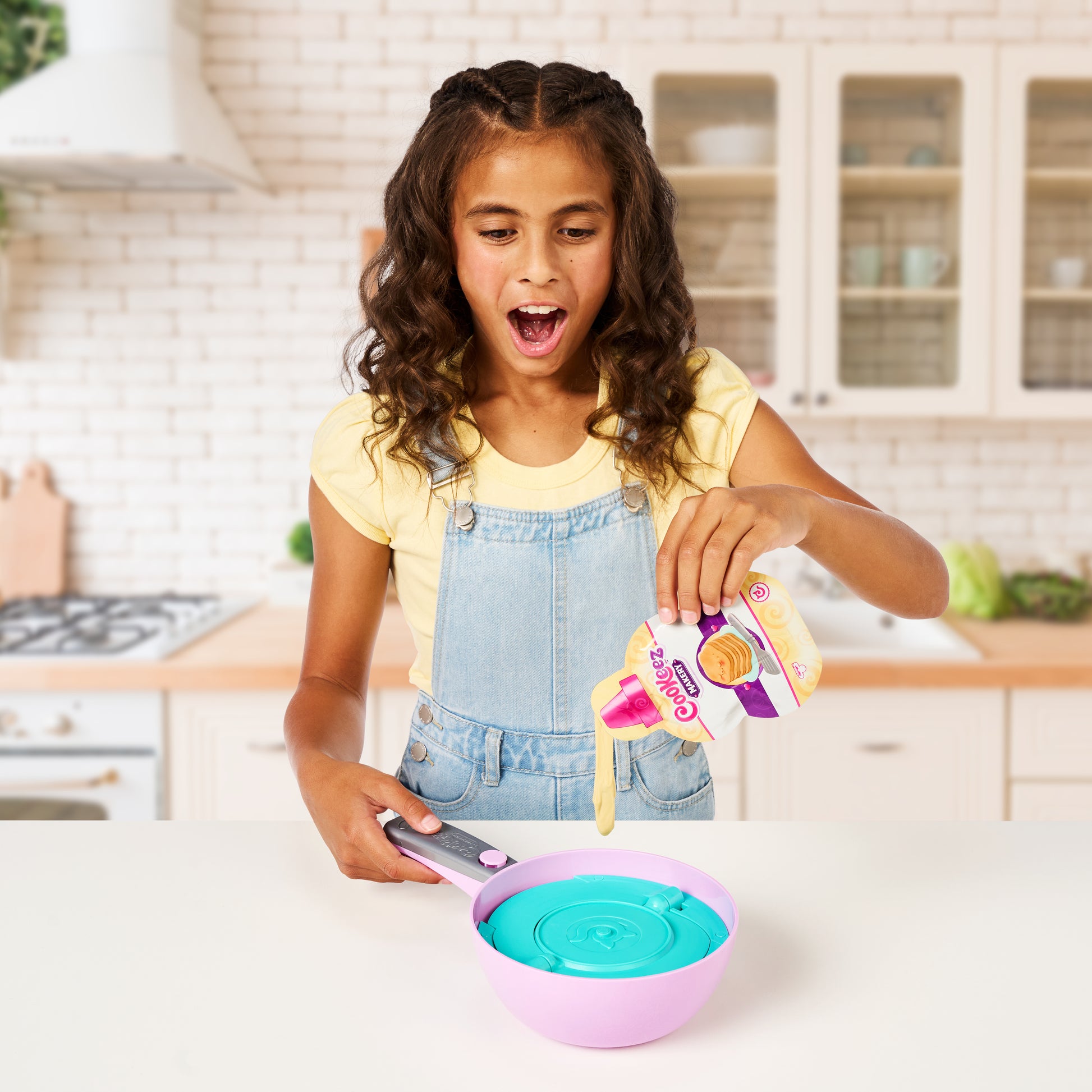 Young girl in a kitchen pouring a colorful toy into a pink and purple bowl.