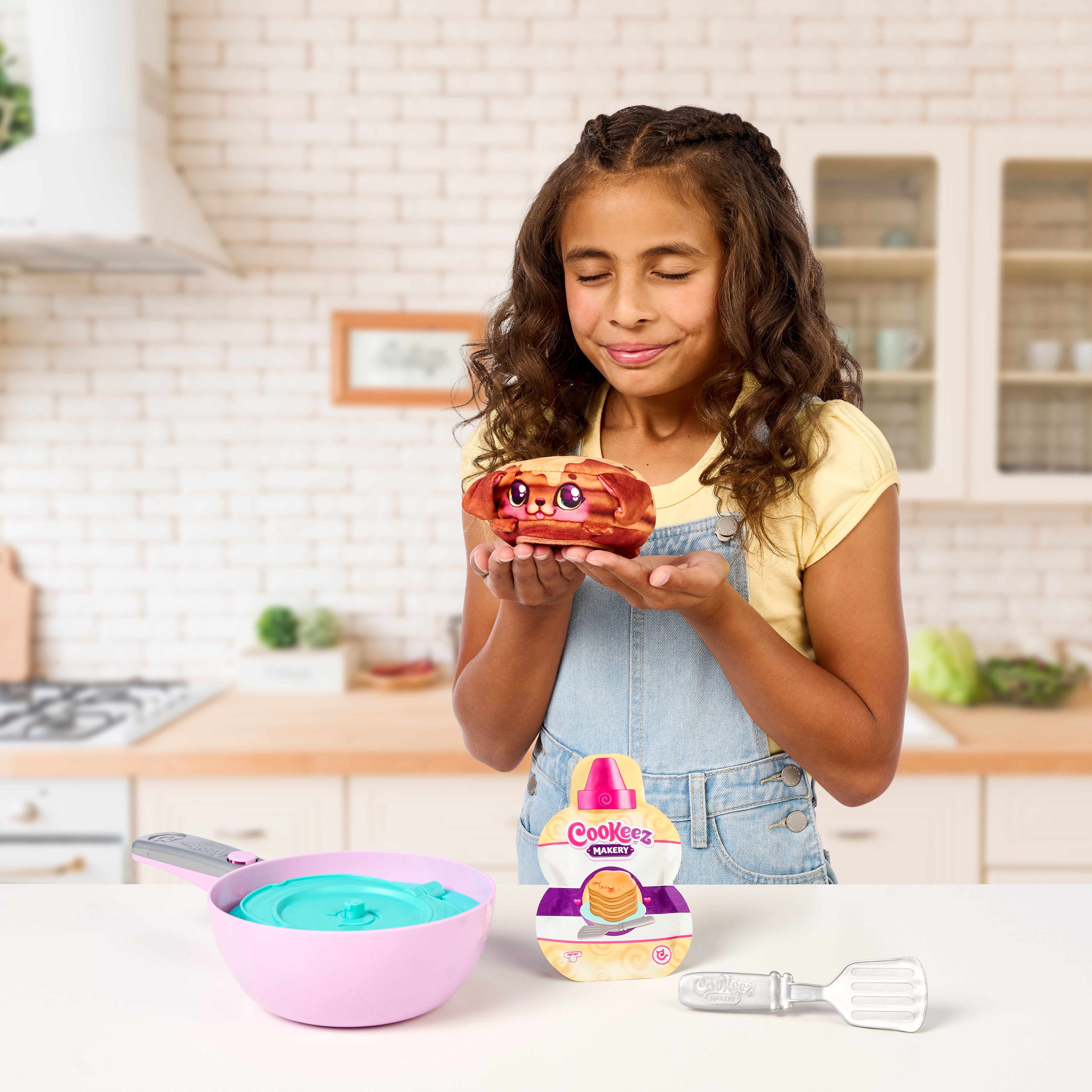 Girl holding a toy kitchen set with a bowl and spatula in a kitchen setting