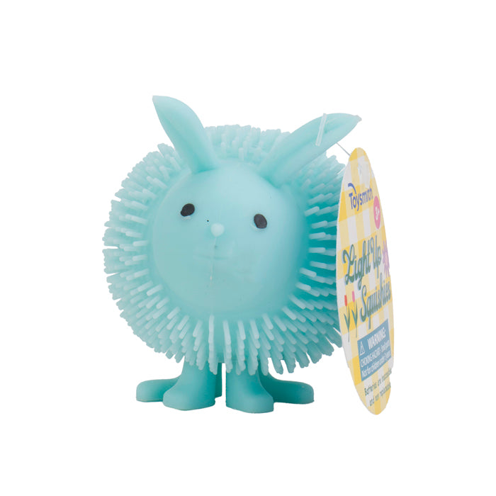 The Toysmith Light Up Squishies by Toysmith is a light blue, spiky rubber toy shaped like a round animal with rabbit ears, small black eyes, and four legs. It features a yellow and white tag and is perfect for sensory play.