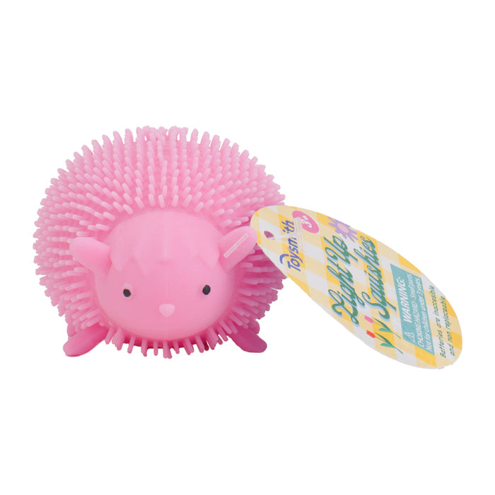 The Toysmith Light-Up Squishies is a pink, round, spiky rubber hedgehog toy with small ears, a snout, and four stubby legs. Perfect for sensory play, it features a vibrant product tag with colorful text and graphics.