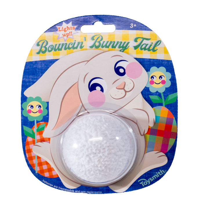 Packaging for Toysmith's Light Up Bunny Tail Ball features a white bunny with pink cheeks, flowers, and a clear bubble showing the glowing fluffy ball inside. Great for Easter baskets. Packaging reads: “Lights Up!”.