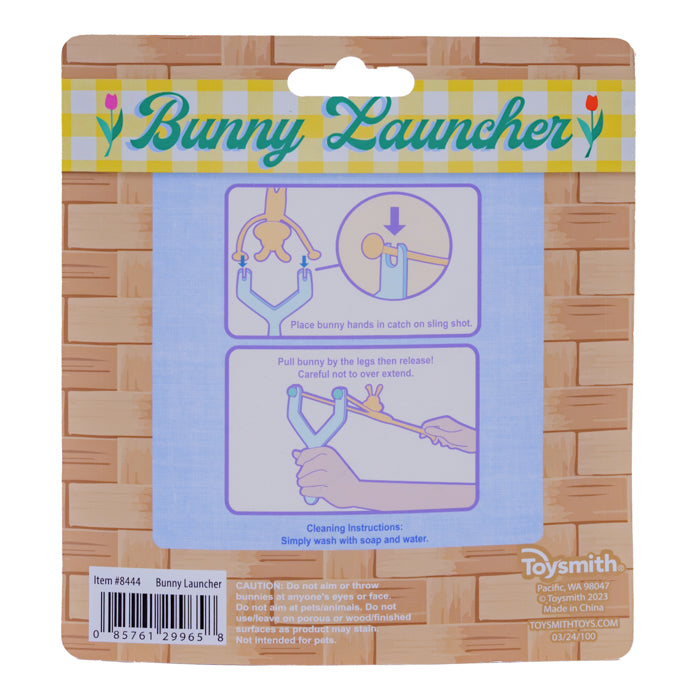 Back of a Toysmith Bunny Launcher package shows illustrated instructions: place bunny in launcher, pull and release to launch. Wash with soap and water. Ideal Easter basket toy. Toysmith brand and barcode appear at the bottom.