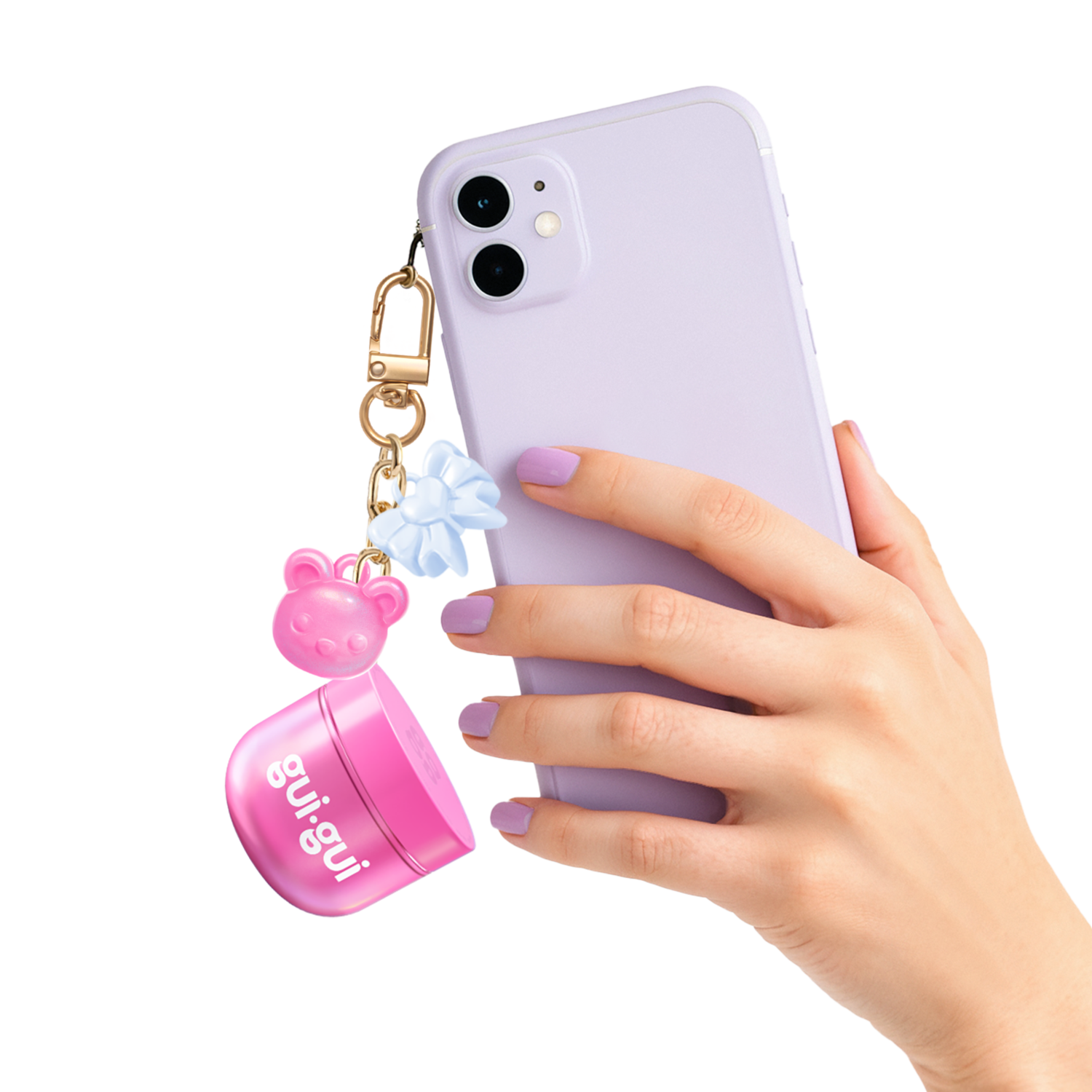 A hand with pastel purple nails holds a lavender smartphone, adorned with a keychain featuring the Moose Toys Gui Gui Mini Backpack Charm Slime, along with a pink bear-shaped charm and blue bow.