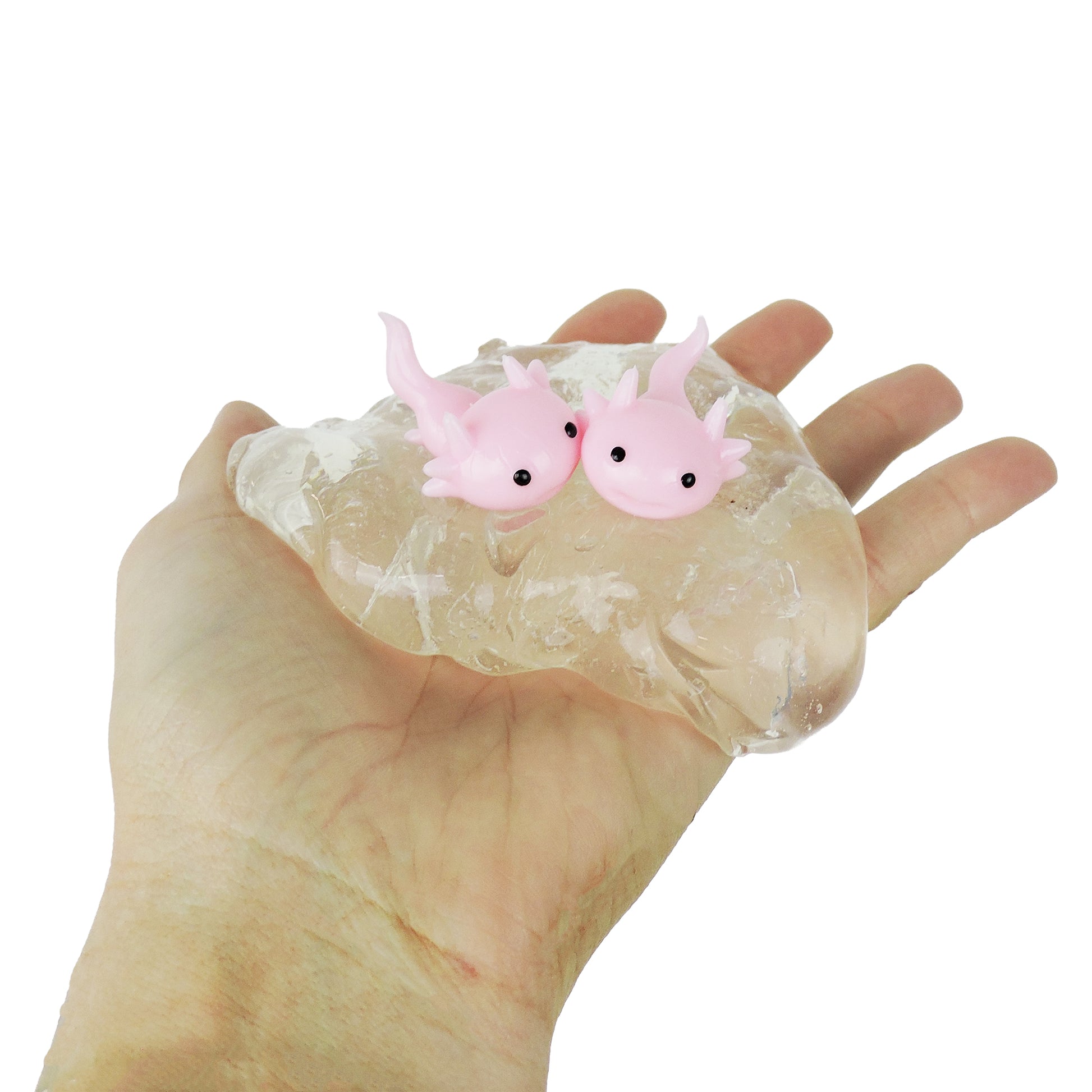 A hand holds a clear slime blob with two Tiny Toys Itty Bitty Axolittles—small pink axolotl squishies with big black eyes and tiny limbs—inside, offering a playful sensory experience.