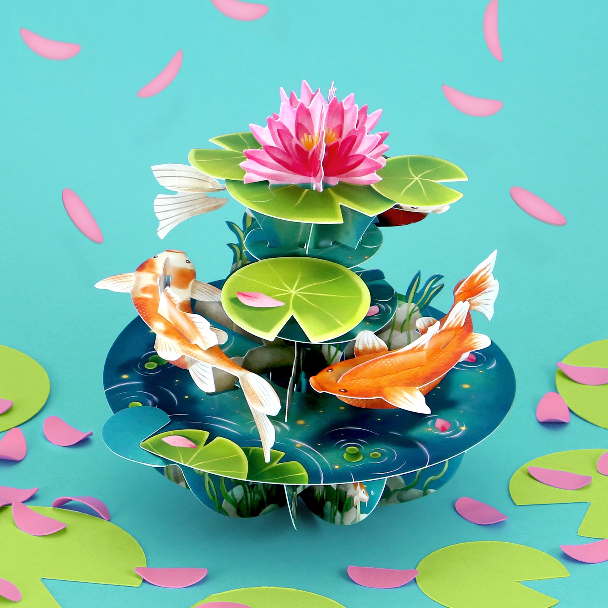 The Santoro Pirouette Card: Koi Carp features a vibrant 3D pond scene with two orange koi fish, green lily pads, a large pink lotus flower, and scattered pink and green petals set against a blue background.