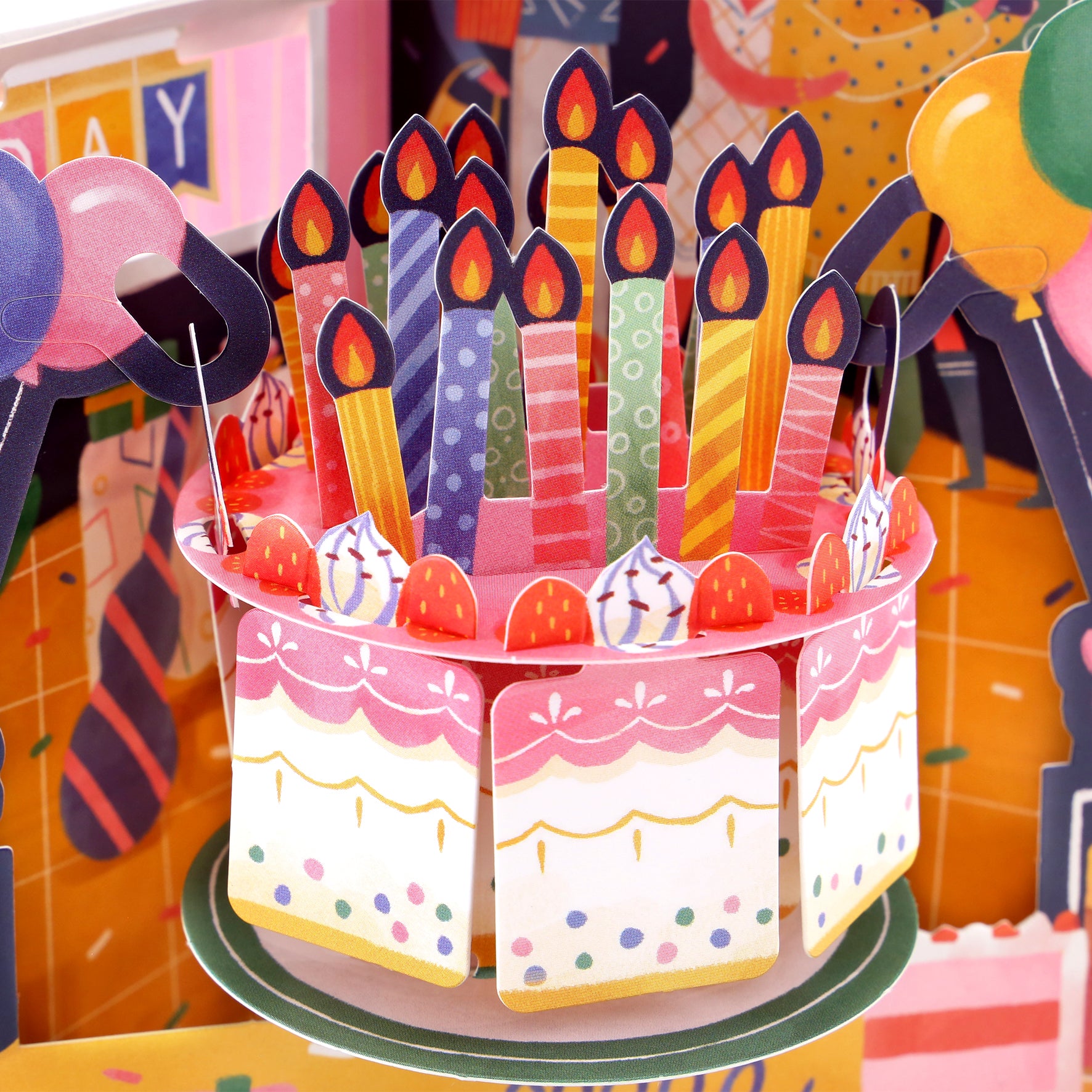 The Santoro Swing Card: Birthday Celebrations features a vibrant pop-up birthday cake adorned with lit candles, strawberries, and swirls, with festive decorations and balloons in the background.