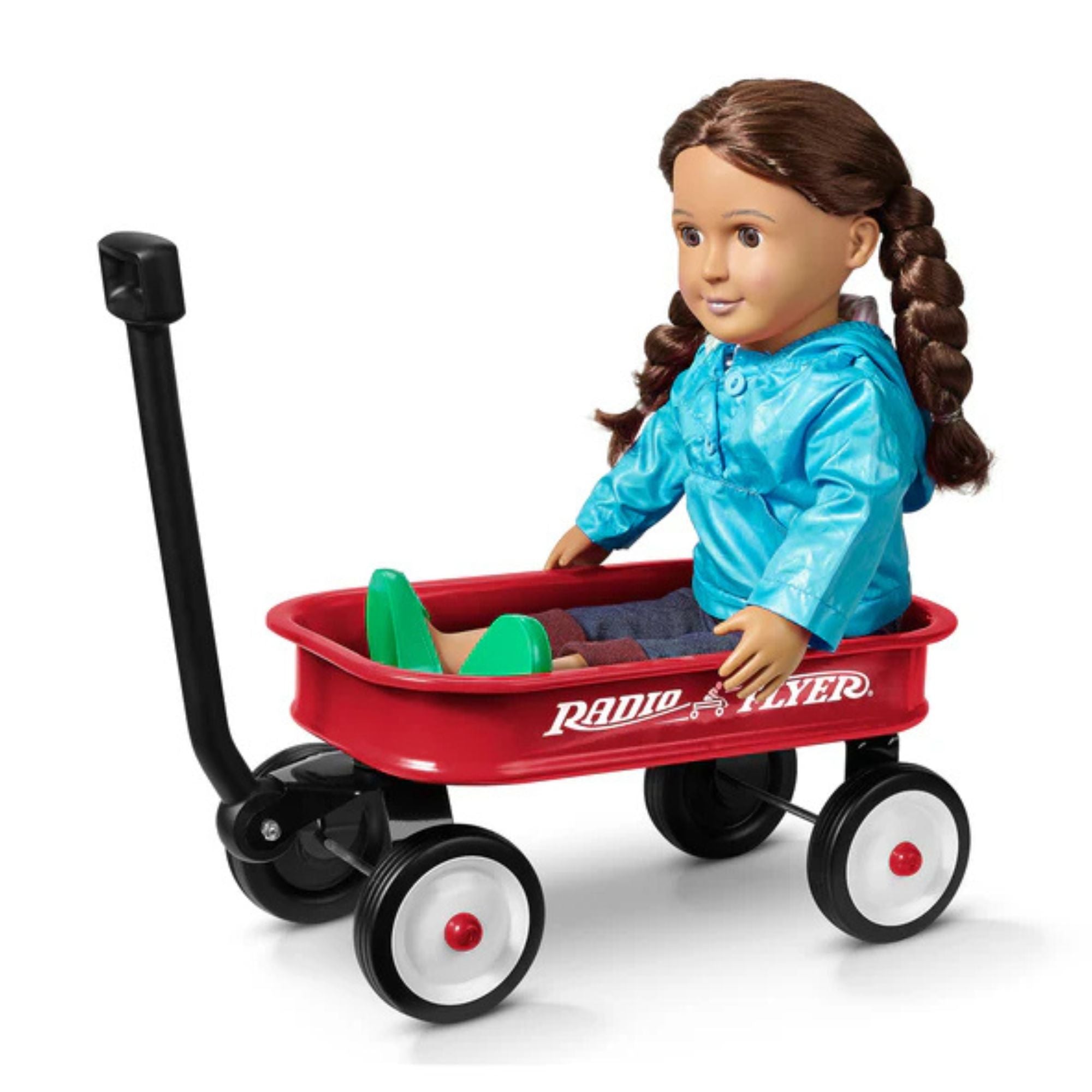 A doll with brown braided hair, dressed in a blue jacket and green shoes, sits in a Radio Flyer Little Red Toy Wagon by Radio Flyer—featuring a black handle and four wheels for imaginative play.
