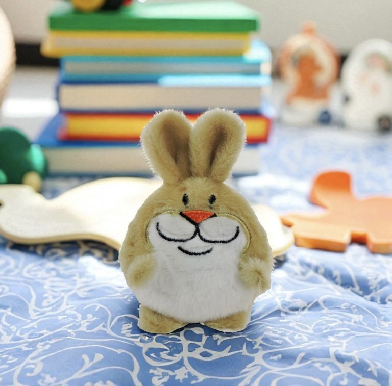 Plush toy rabbit on a blue patterned surface with books and toys in the background